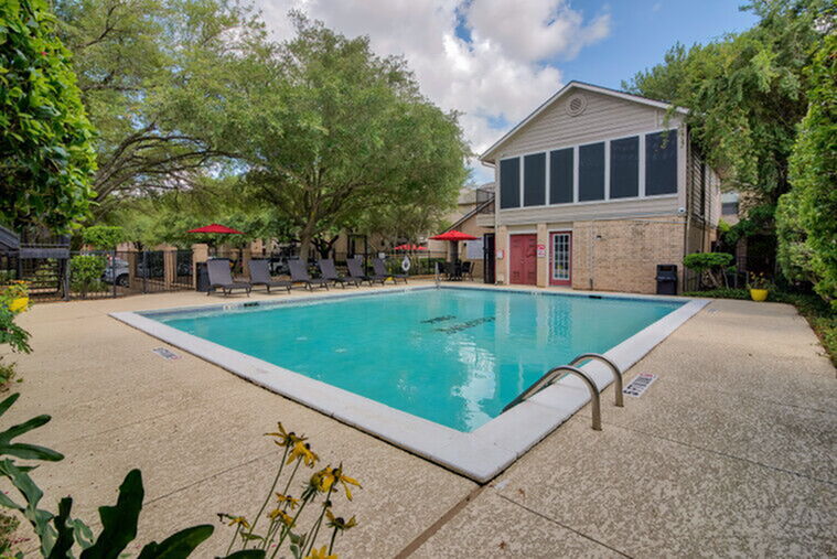 Inviting outdoor pool area with comfortable lounge chairs, surrounded by lush greenery and a charming clubhouse.
