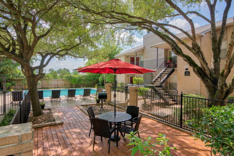 Charming outdoor patio with a red umbrella and stylish furniture, overlooking a sparkling pool surrounded by lush greenery, offering a perfect oasis for relaxation and entertainment.