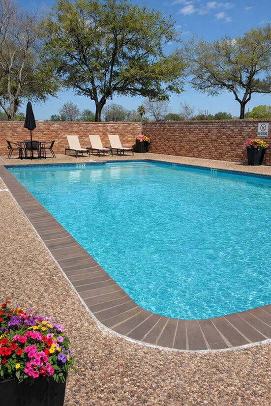 Inviting outdoor pool area with lounge chairs and a patio dining set, surrounded by lush trees and vibrant flowers, perfect for relaxation.