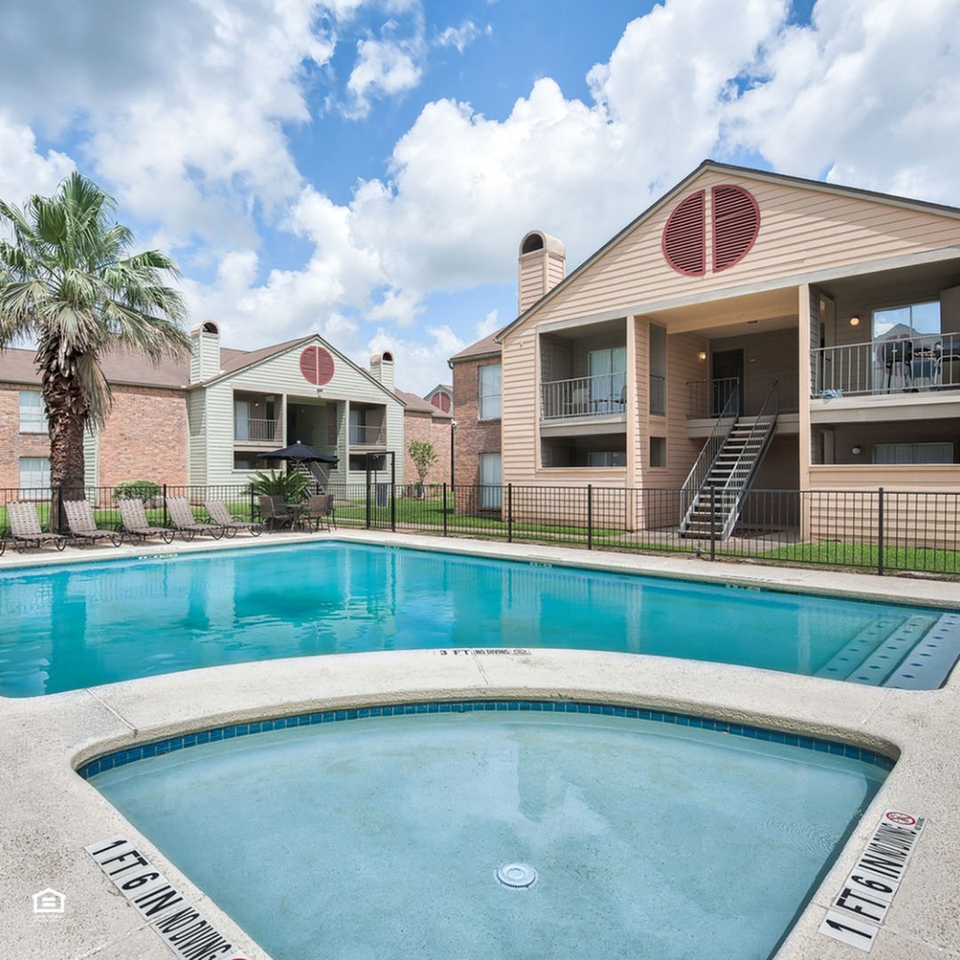 Inviting apartment complex features modern architecture with private balconies overlooking a pristine swimming pool surrounded by lush greenery and palm trees.