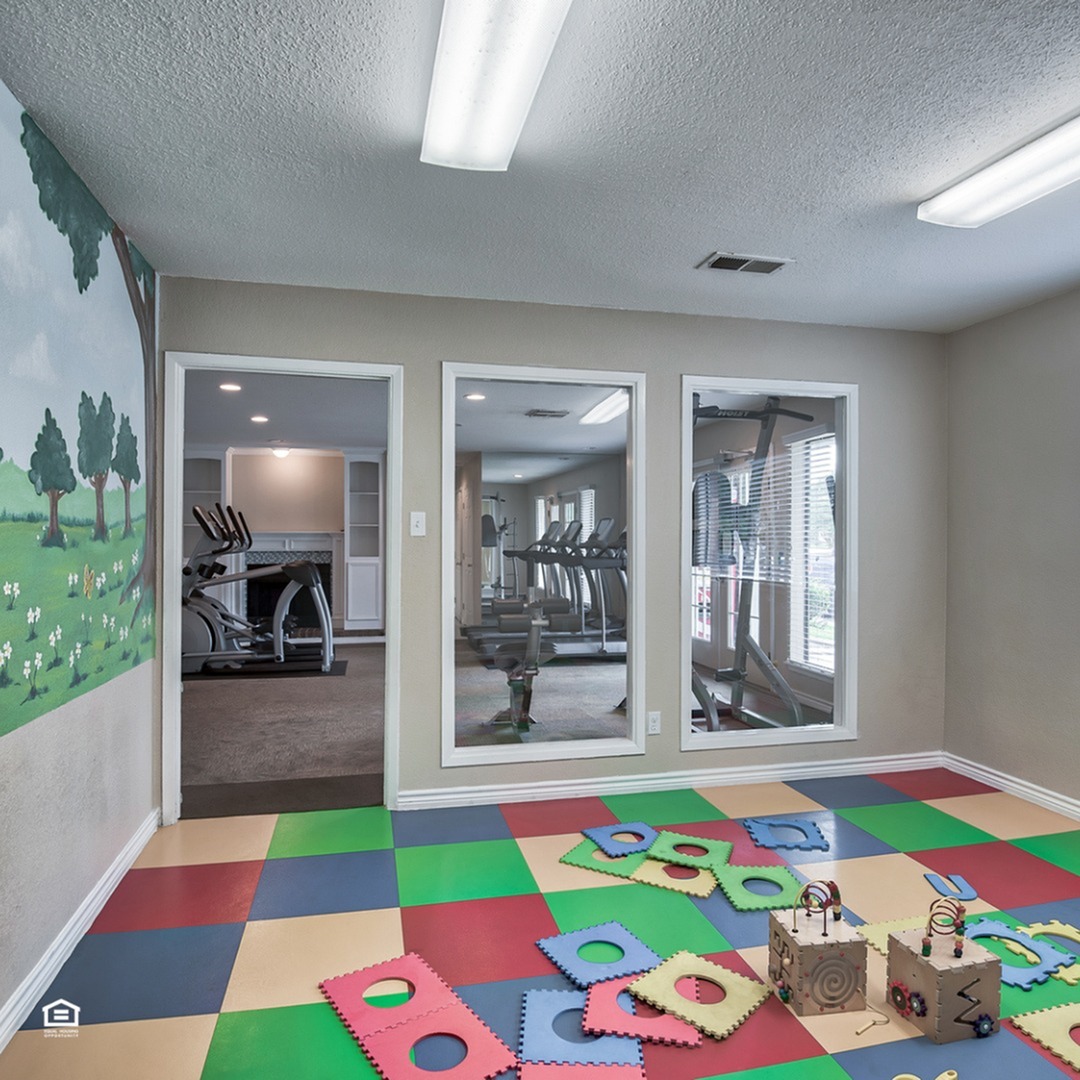 Bright and welcoming multifunctional space with colorful kids\' play area and adjacent fitness room with modern exercise equipment.