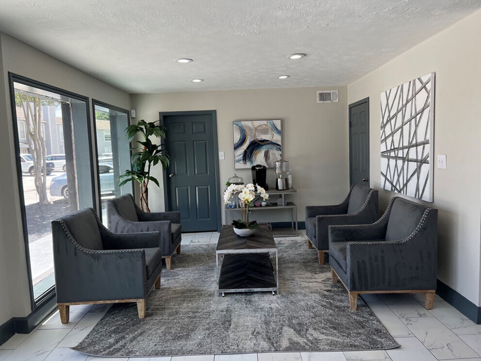Bright and modern lounge area with sleek gray armchairs, elegant artwork, and abundant natural light through large windows.