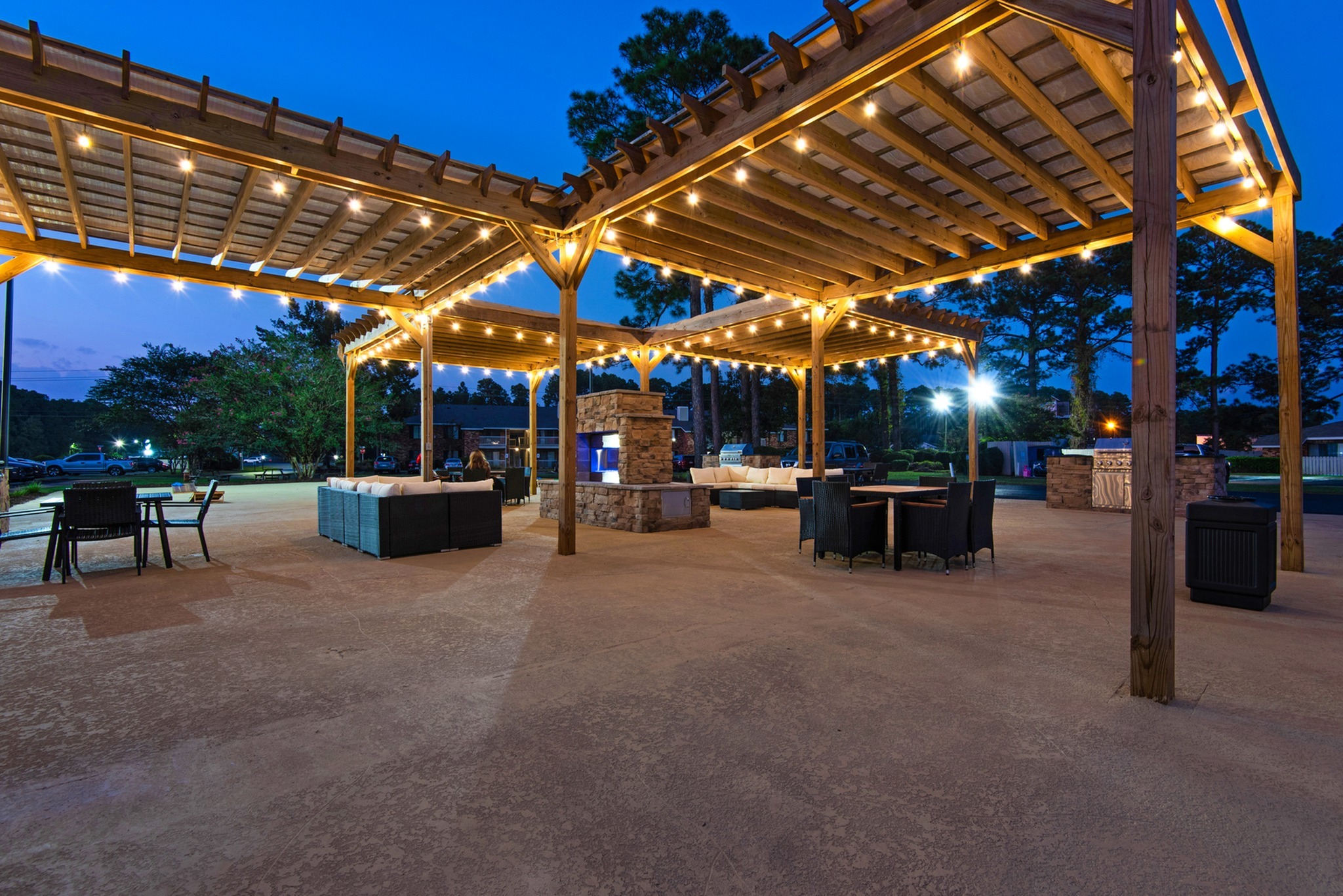 Charming outdoor patio at twilight featuring elegant pergola lighting, cozy seating, and a stone fireplace, perfect for evening gatherings in a tranquil setting.