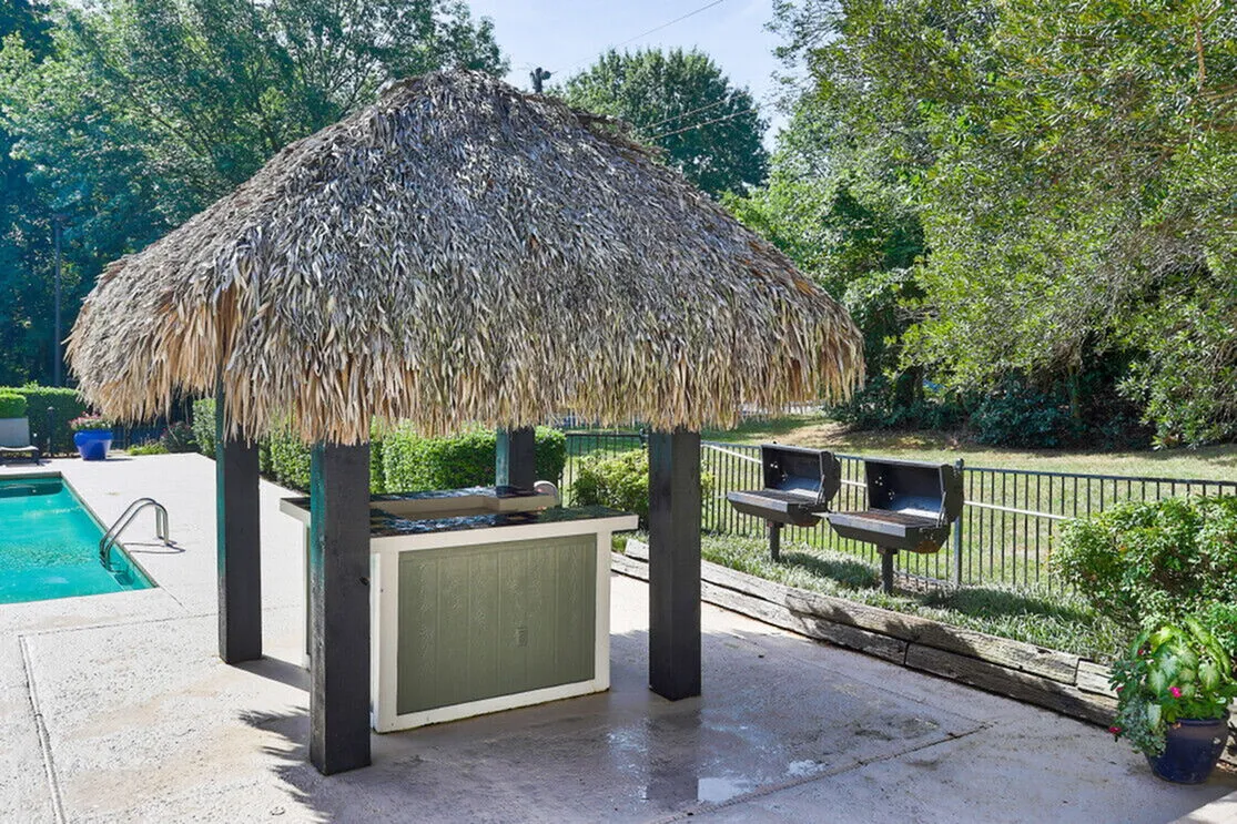 Charming poolside oasis with a thatched-roof bar, nestled amidst lush greenery, offering leisure and relaxation.