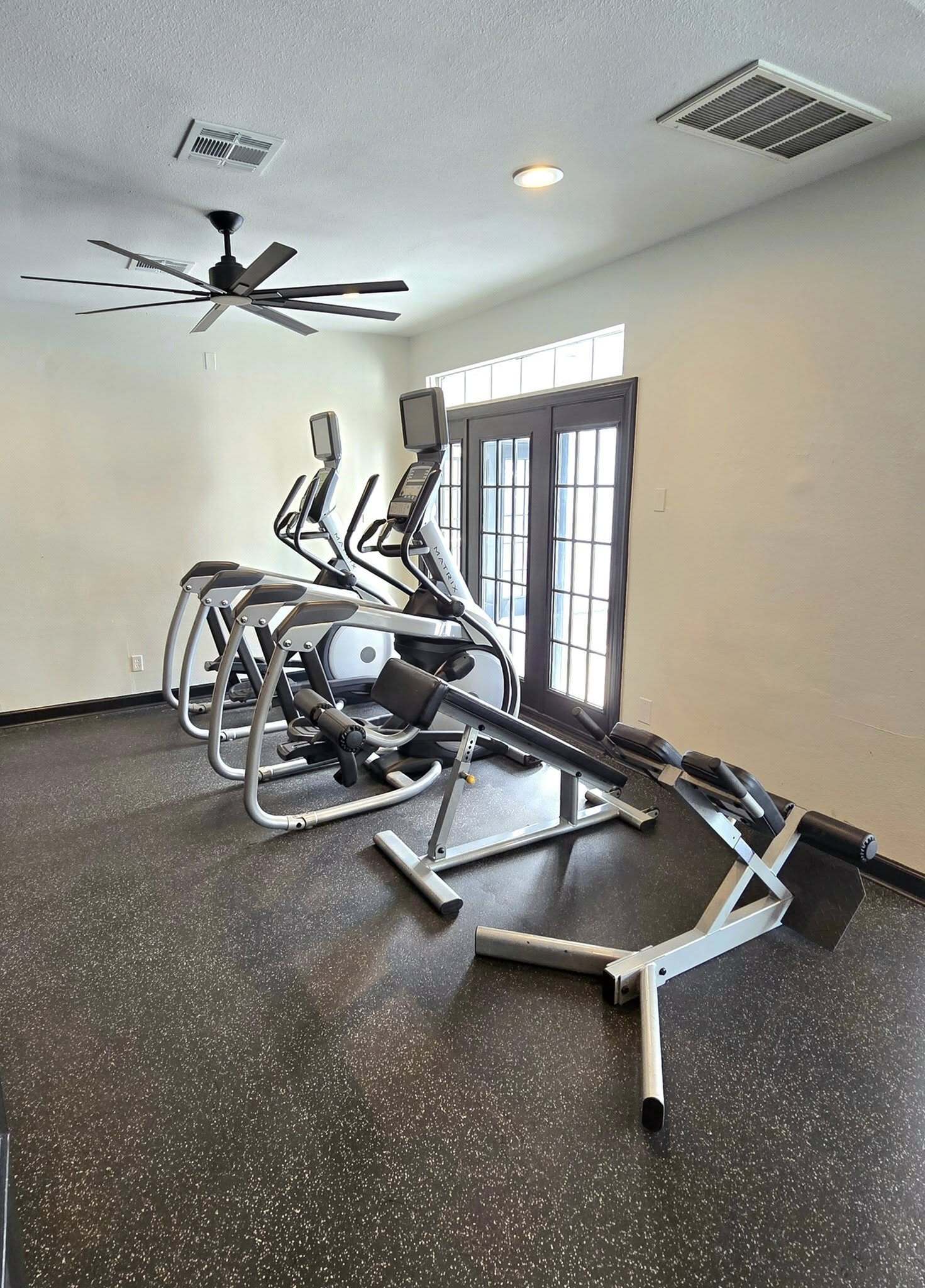 Bright and modern gym with state-of-the-art exercise equipment, featuring elliptical machines under stylish ceiling fan lighting.