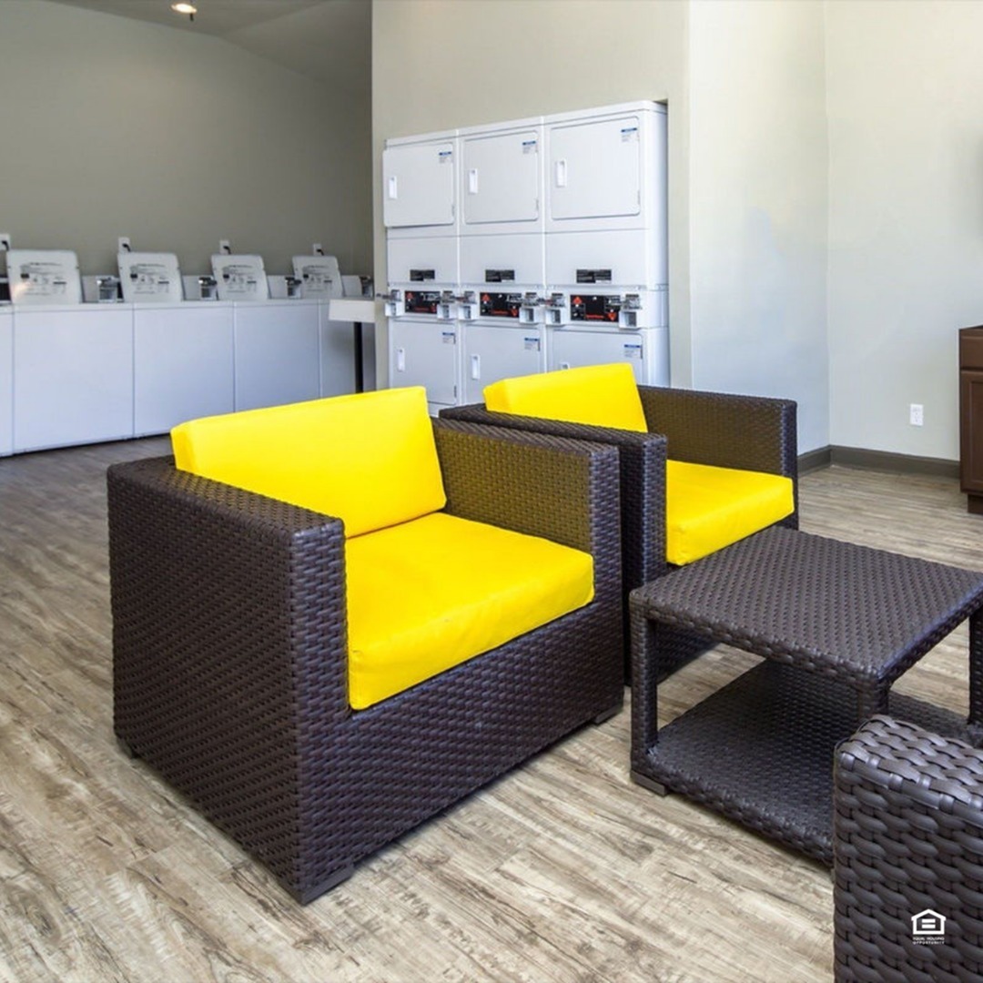 Modern laundry room with vibrant yellow cushioned wicker chairs and stacked washing machines.