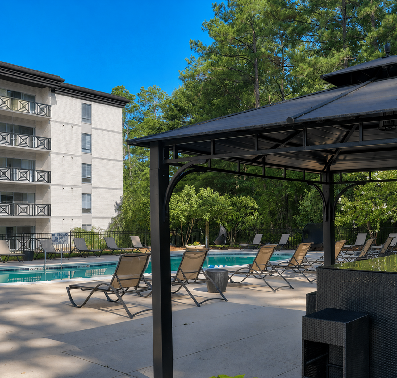 Luxurious apartment complex with pristine poolside lounge chairs and a stylish outdoor gazebo, surrounded by lush greenery.