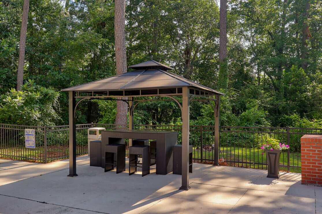Charming outdoor gazebo with modern furniture set amidst lush greenery, perfect for relaxation and entertaining.