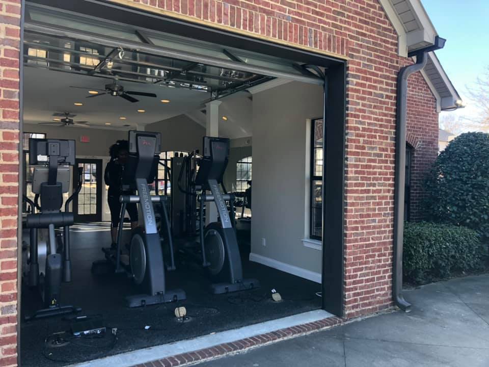 Modern gym facility with state-of-the-art exercise machines, featuring an open garage-like entrance and stylish brick exterior.