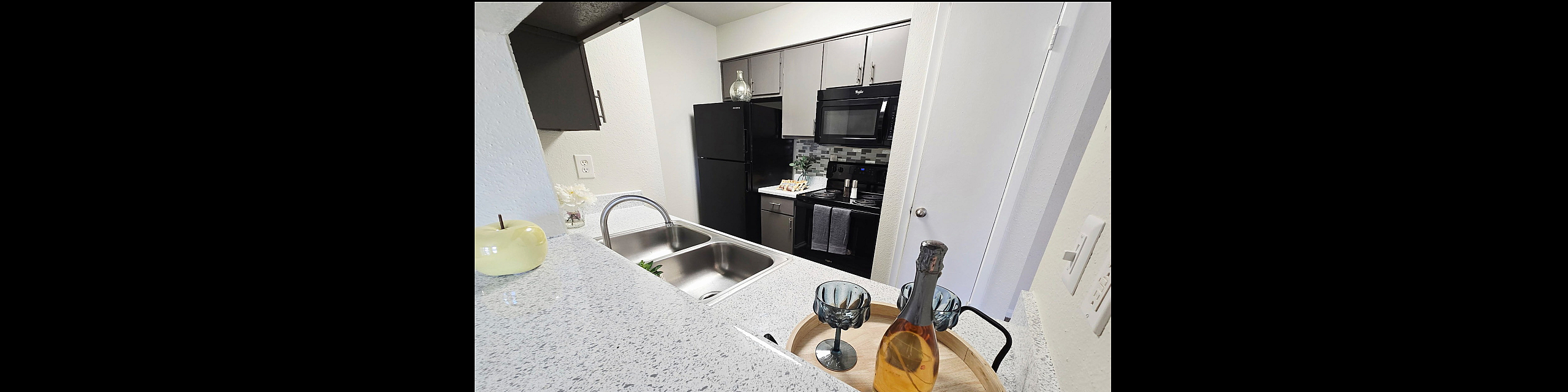 Modern kitchen with sleek countertops, stainless steel sink, and stylish appliances, featuring a cozy dining nook with elegant glassware and a bottle of wine.