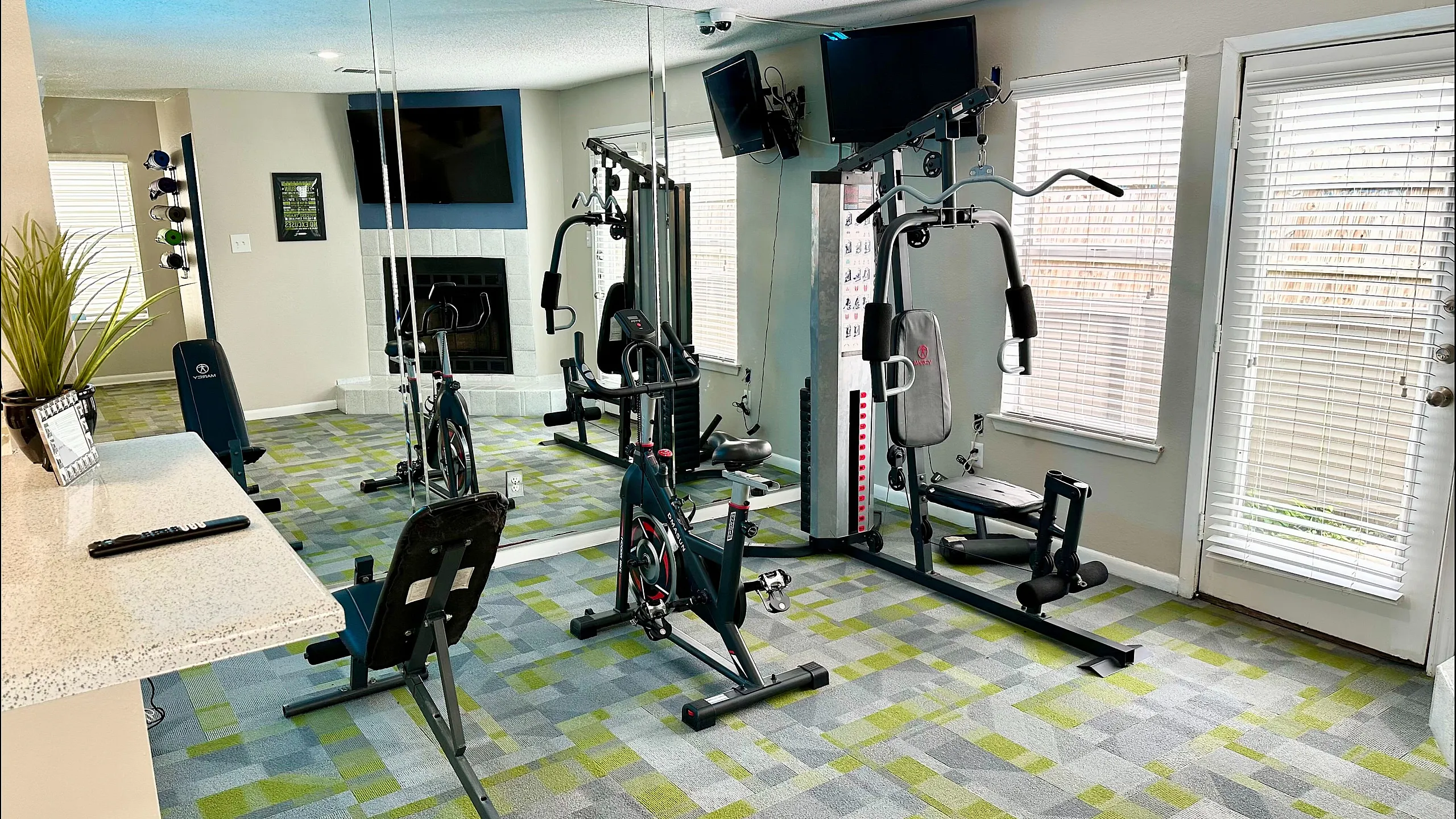 Chic apartment gym with modern exercise equipment, vibrant carpet, and a cozy fireplace, perfect for a stylish lifestyle.