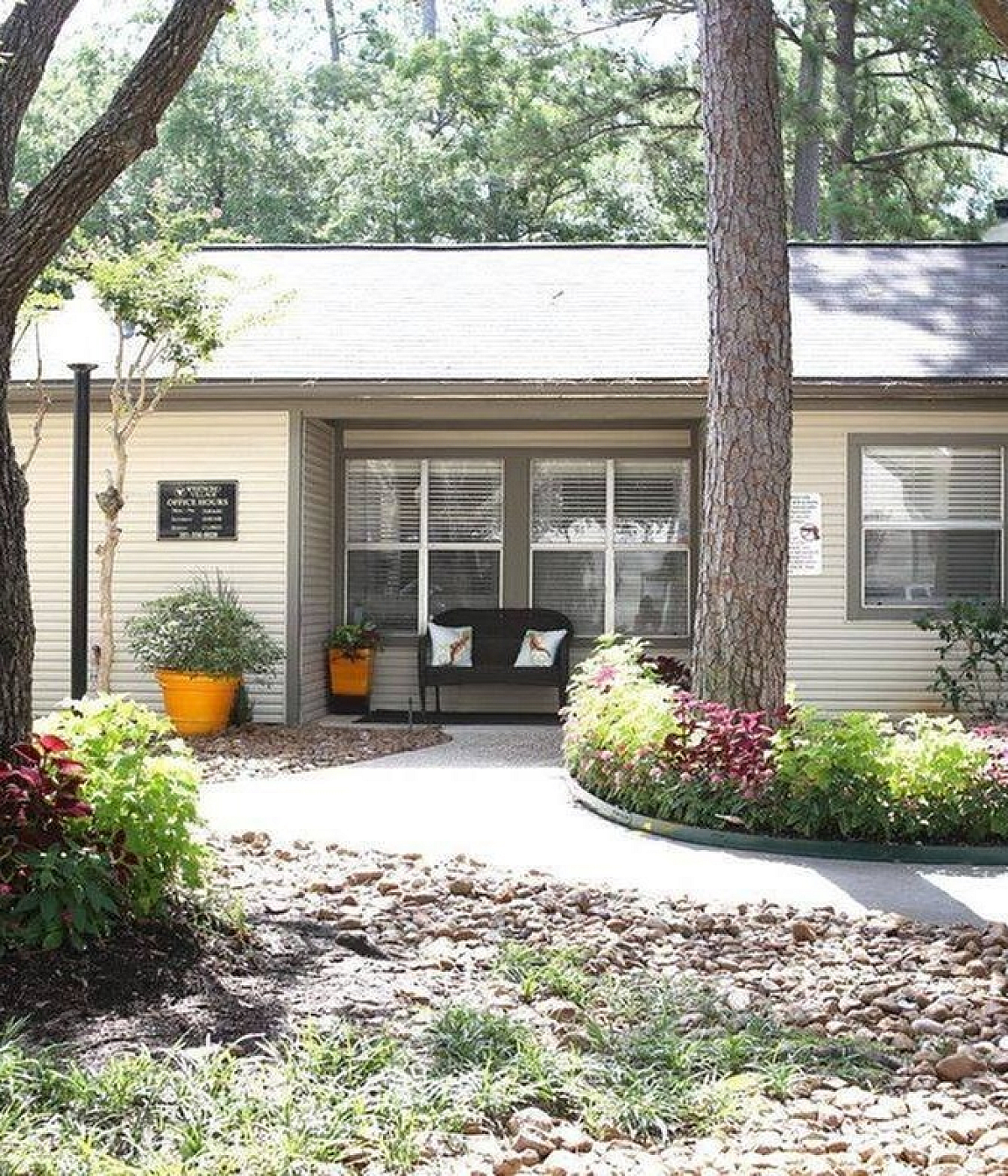 Charming single-story house surrounded by lush greenery and vibrant potted plants, featuring a welcoming front porch with inviting seating area.