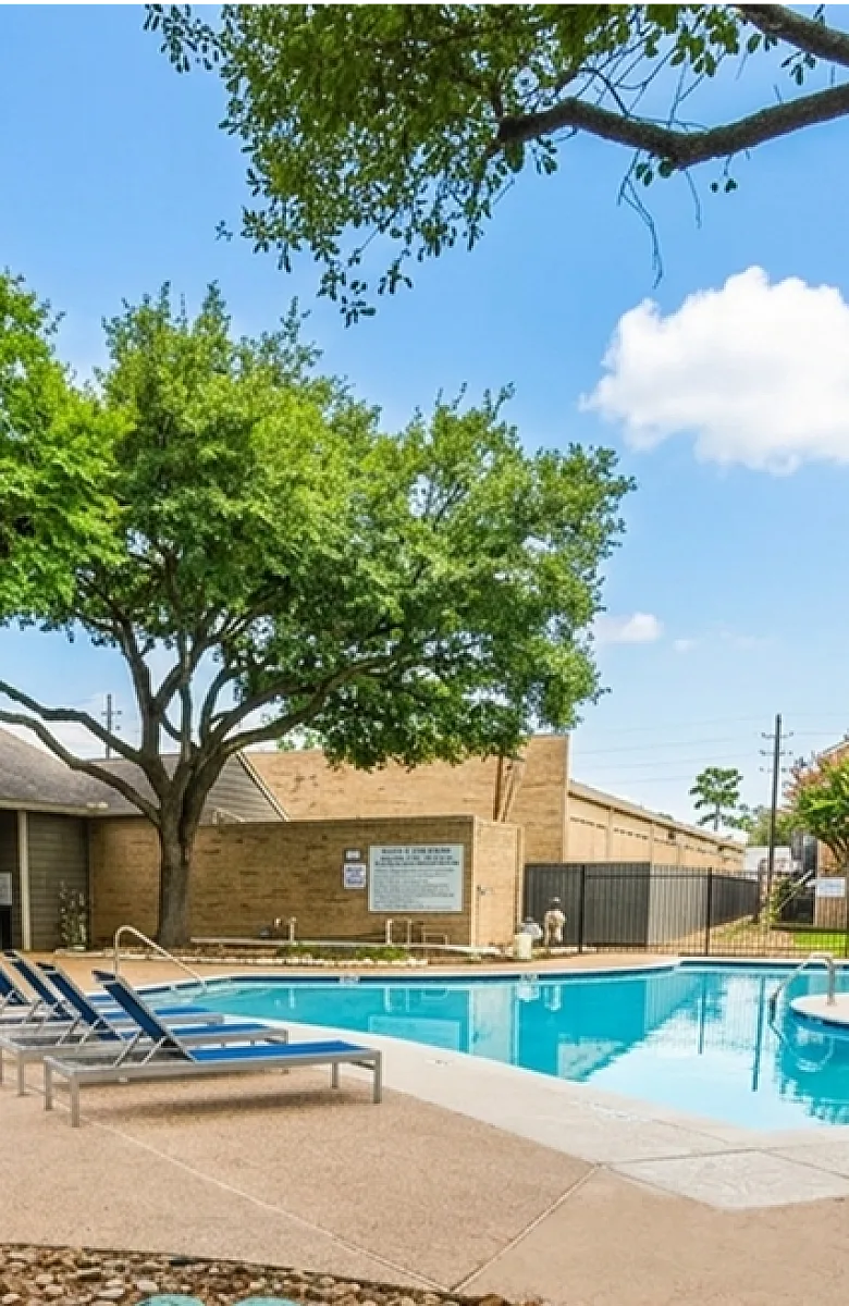 Inviting apartment complex with a sparkling outdoor pool surrounded by lush greenery and stylish lounge seating.