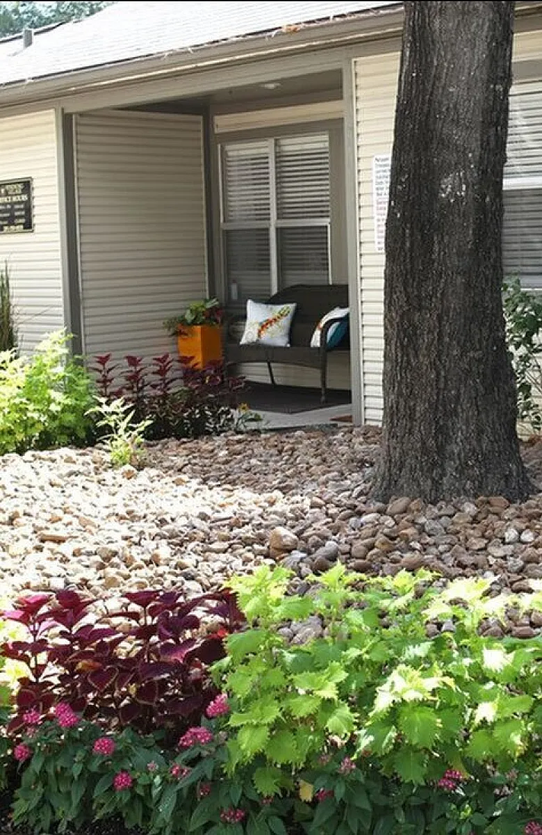 Charming apartment exterior featuring a cozy porch, vibrant landscaping, and lush greenery, offering serene outdoor living.
