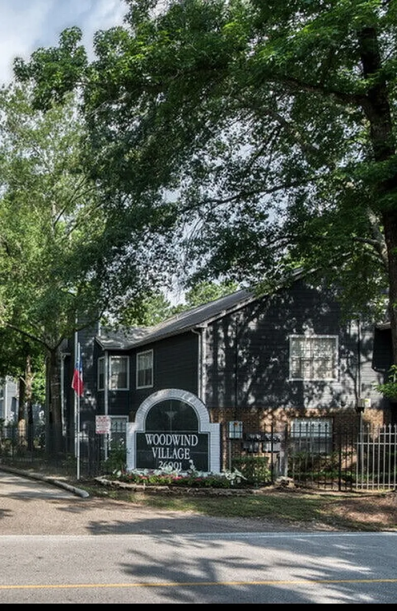 Charming entrance to Woodwind Village with lush greenery and welcoming architecture, offering a serene living environment.