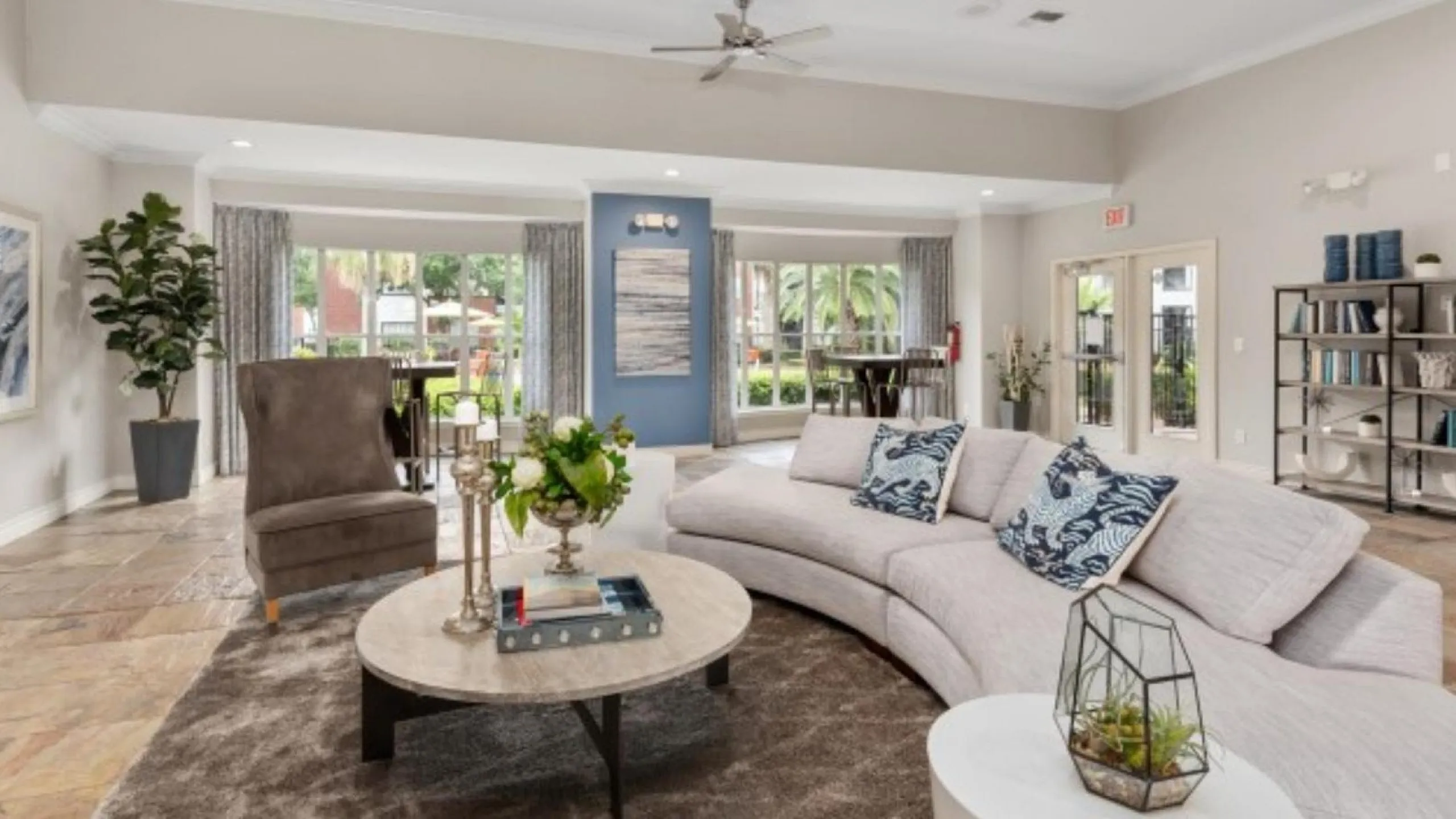 Elegant open living room with contemporary d&eacute;cor, featuring a plush curved sofa, stylish armchair, and floor-to-ceiling windows with a garden view.