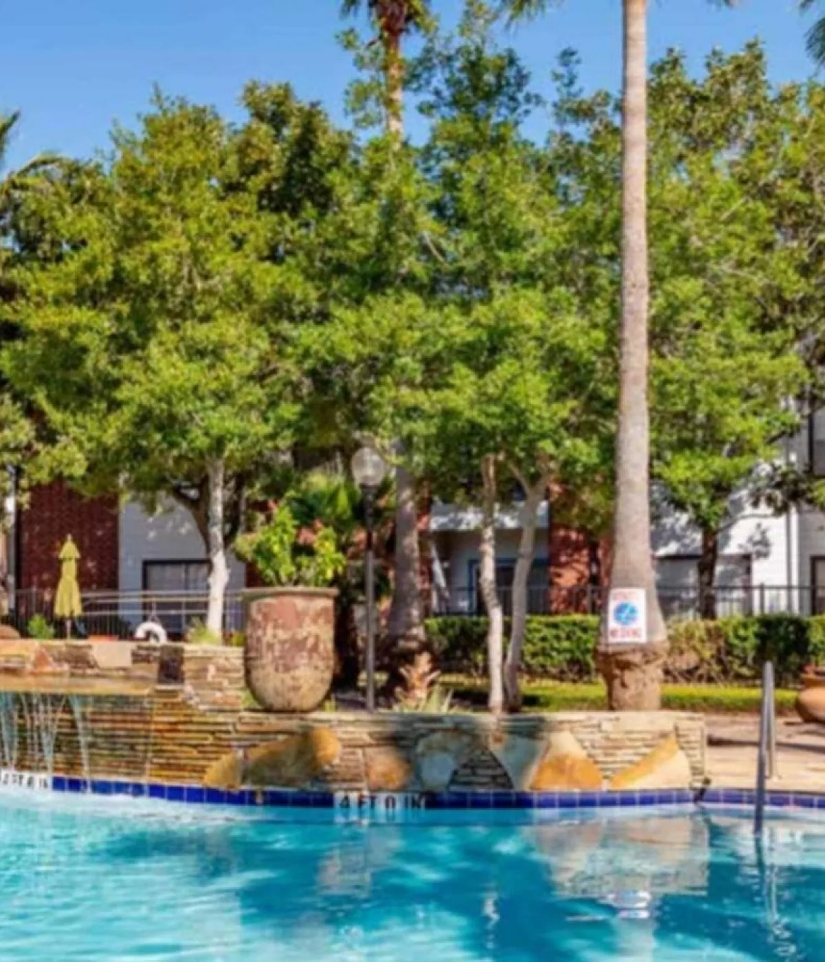 Luxury apartment complex showcasing a sparkling pool with elegant water features and lush palm trees, perfect for relaxation.