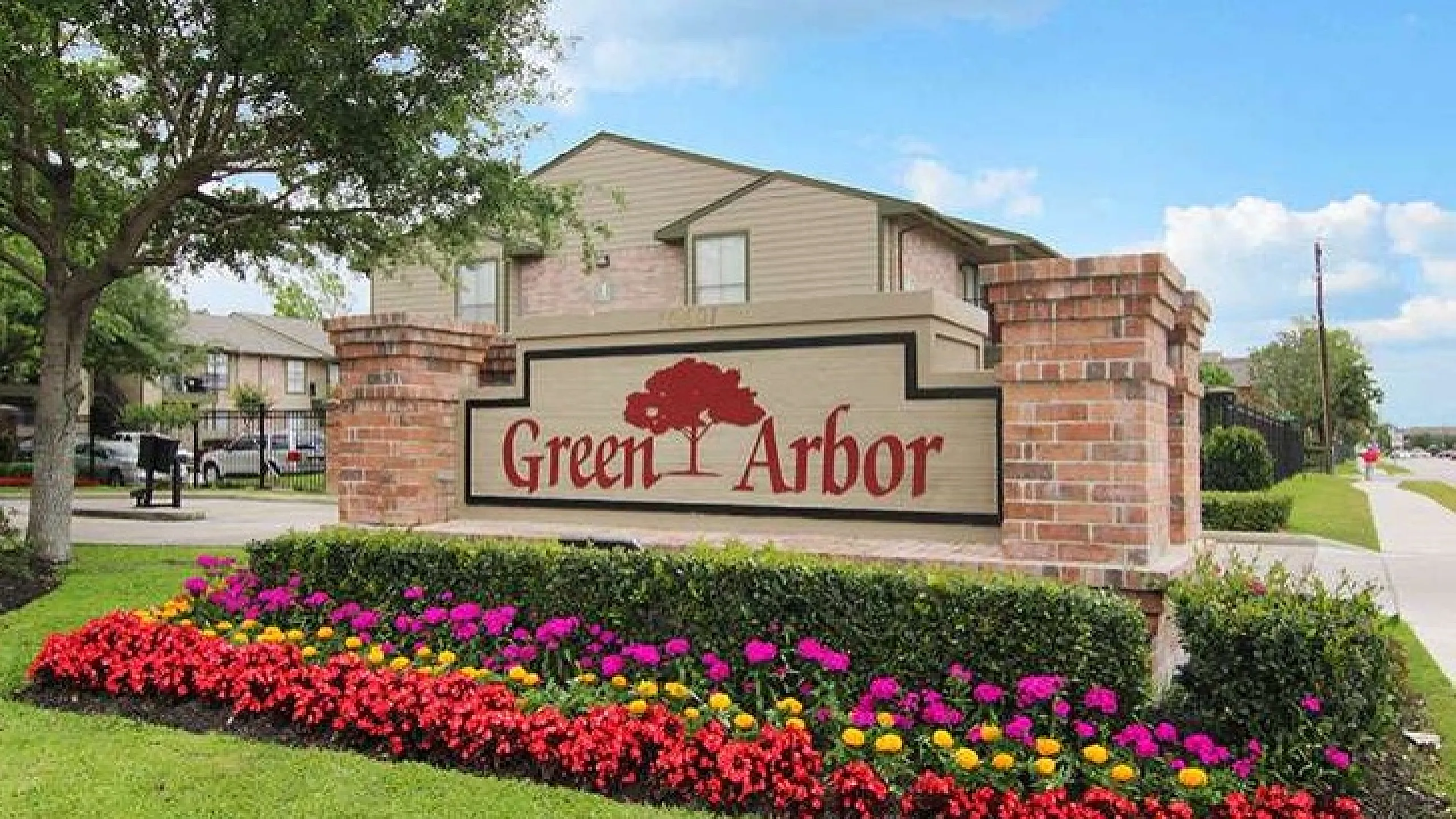 Inviting entrance to Green Arbor Apartments with vibrant flower beds and elegant brick signage.