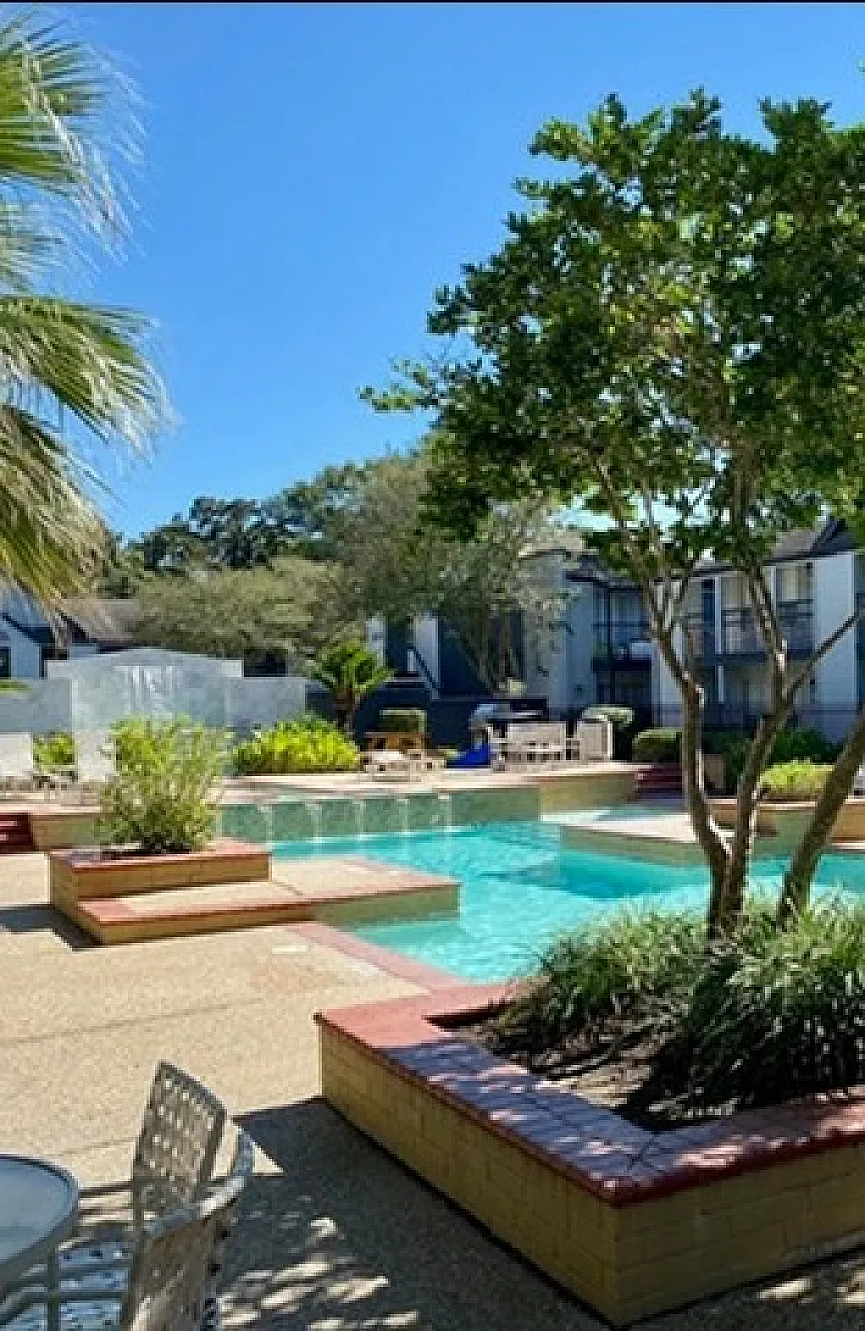 Charming outdoor swimming pool area surrounded by lush greenery and elegant seating in a tranquil apartment complex setting.