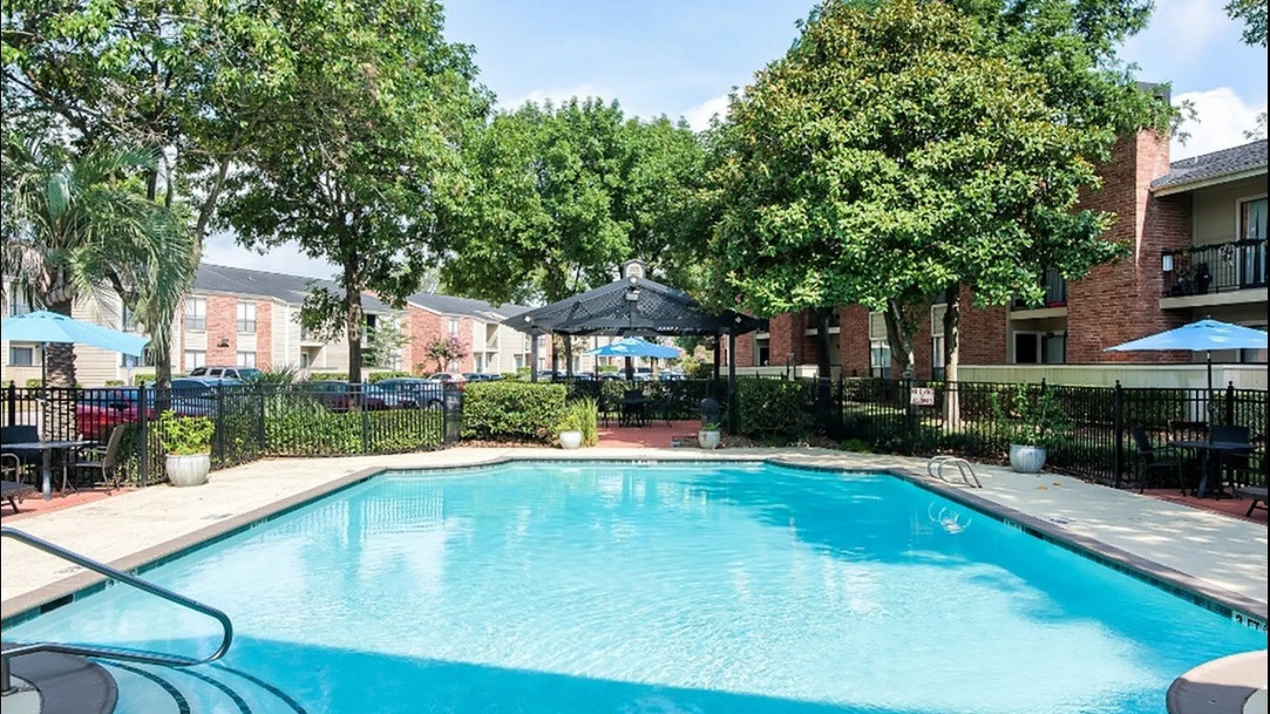 Inviting apartment community swimming pool surrounded by lush greenery and stylish outdoor seating, perfect for relaxation and socializing.