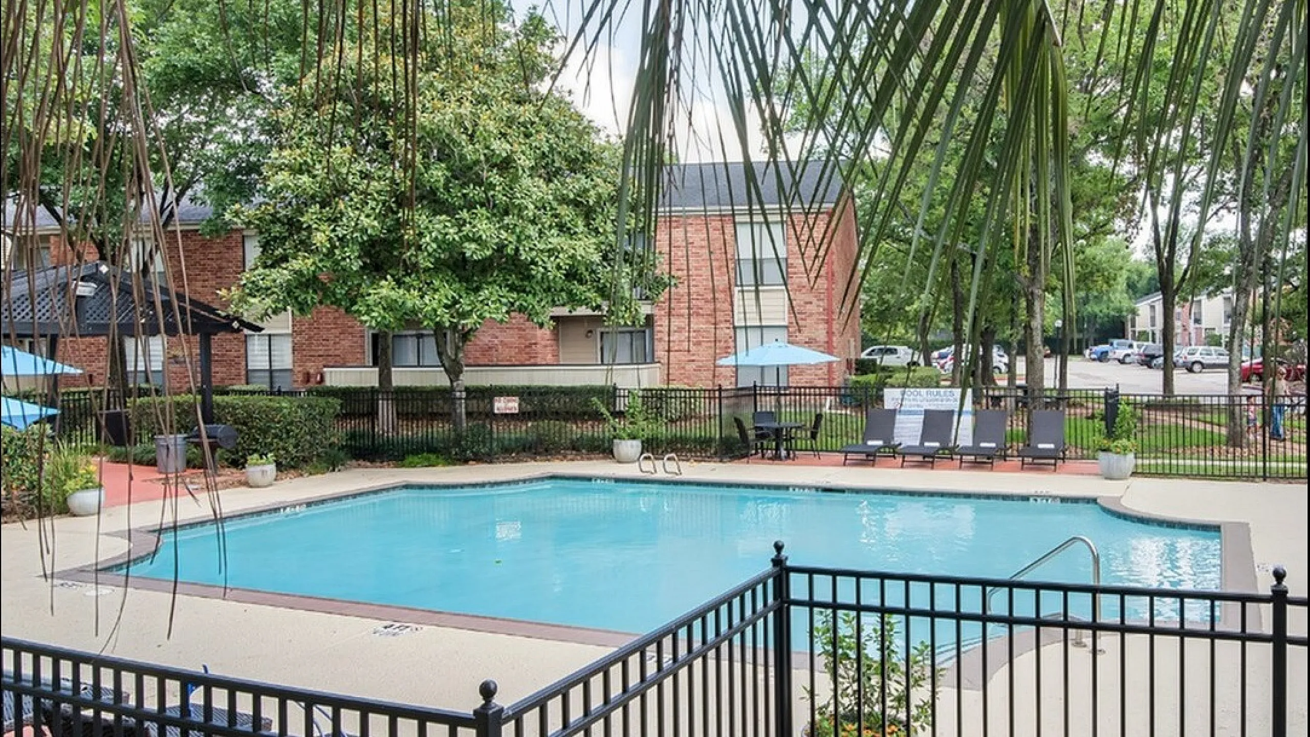 Inviting apartment complex courtyard featuring a sparkling swimming pool surrounded by lush greenery and comfortable lounge chairs.