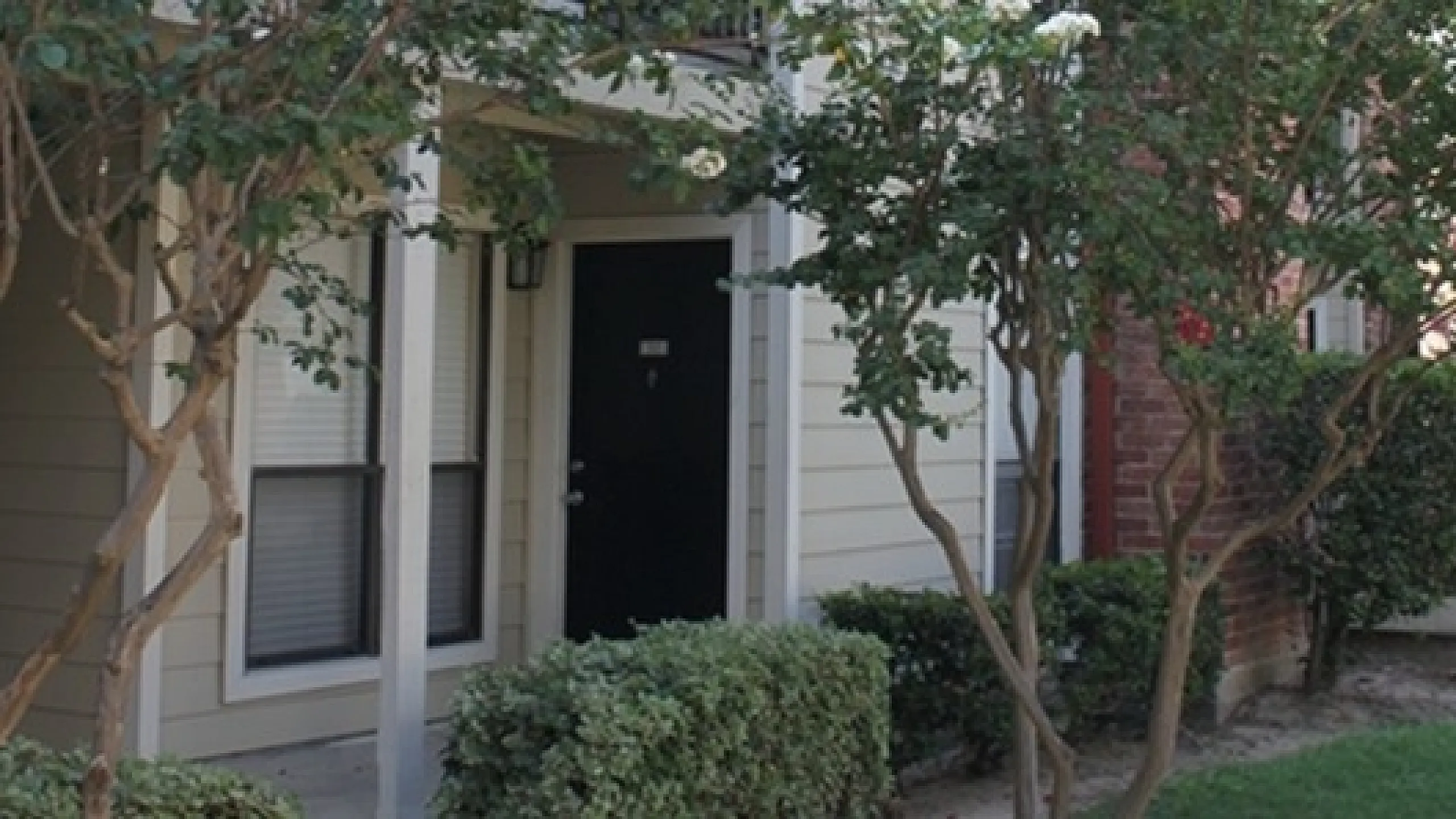Charming apartment exterior with lush greenery and blooming trees, offering a serene and inviting entrance.