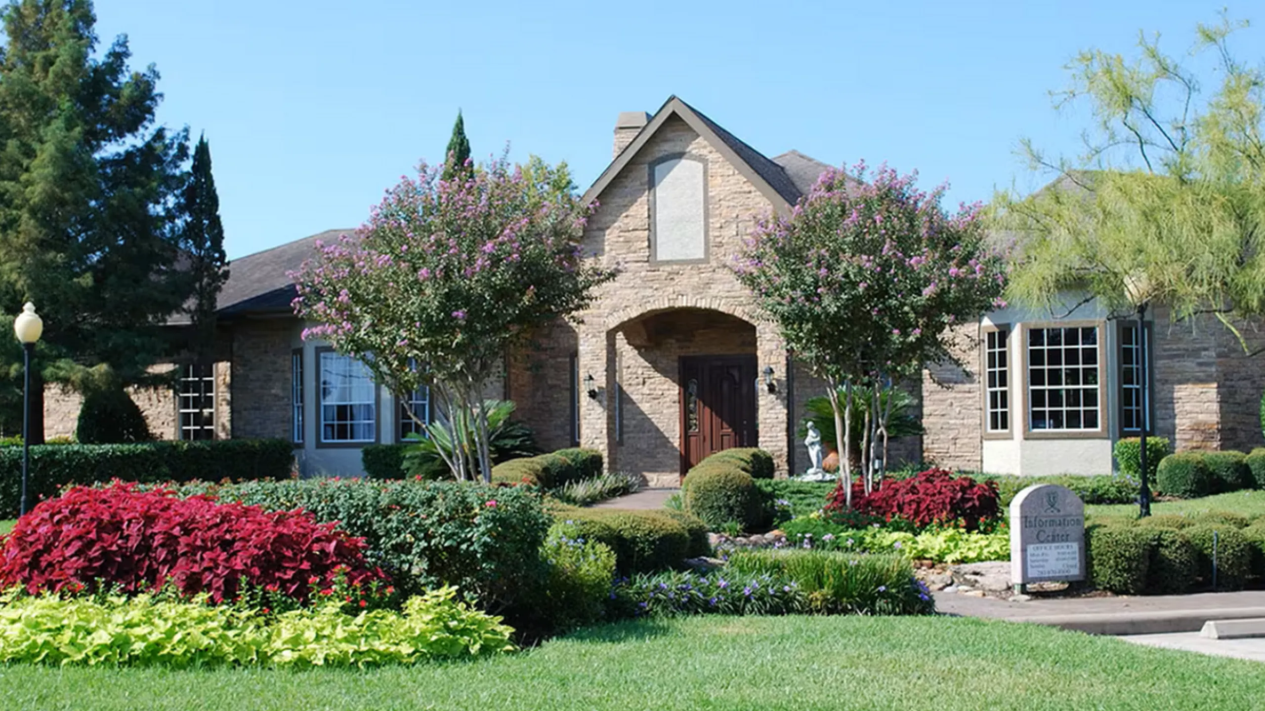 Charming single-story home with stone exterior, vibrant garden, and lush green lawn, offering a warm and inviting curb appeal.