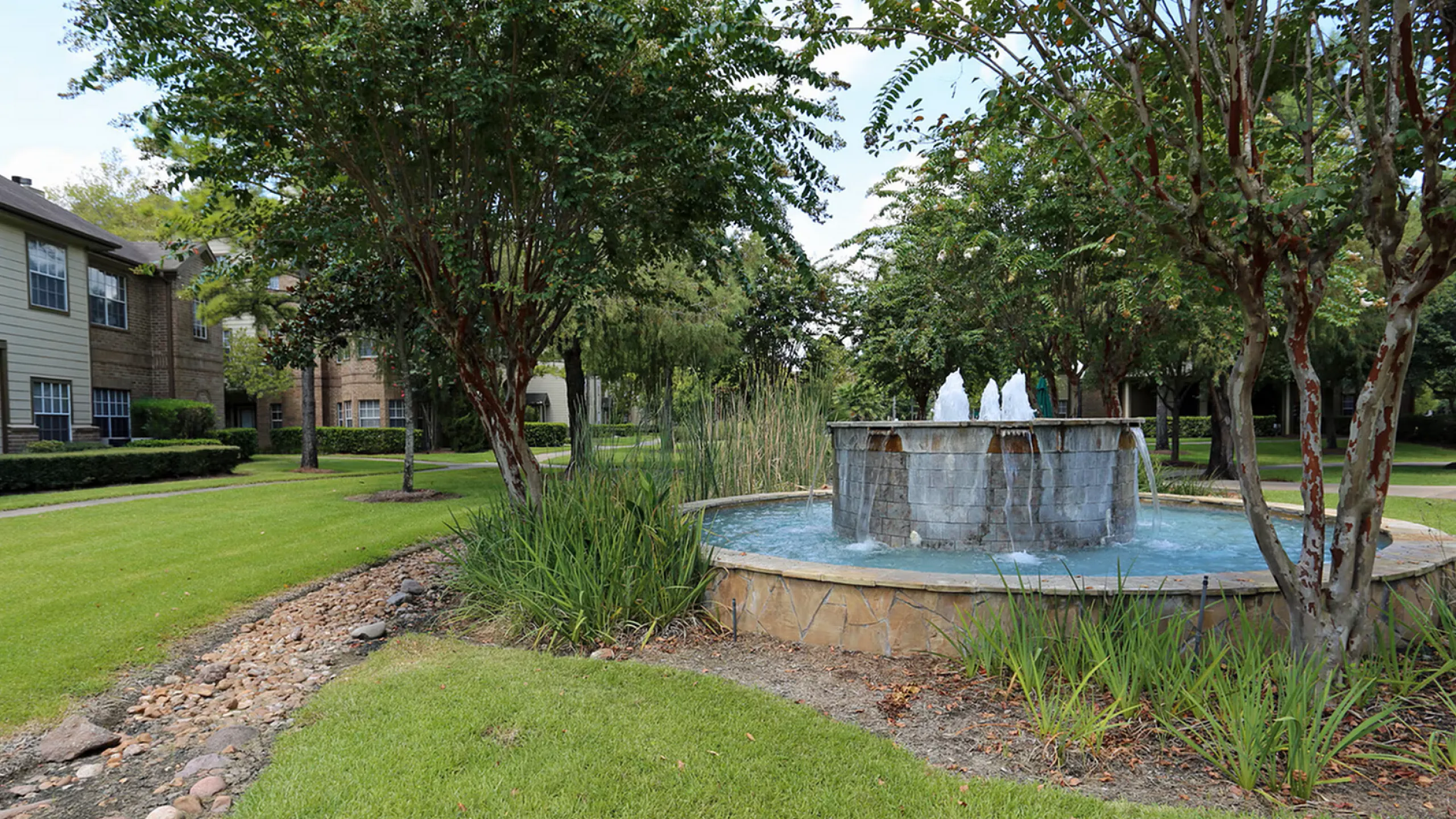 Charming garden setting with a peaceful fountain surrounded by lush greenery and stylish apartment buildings.
