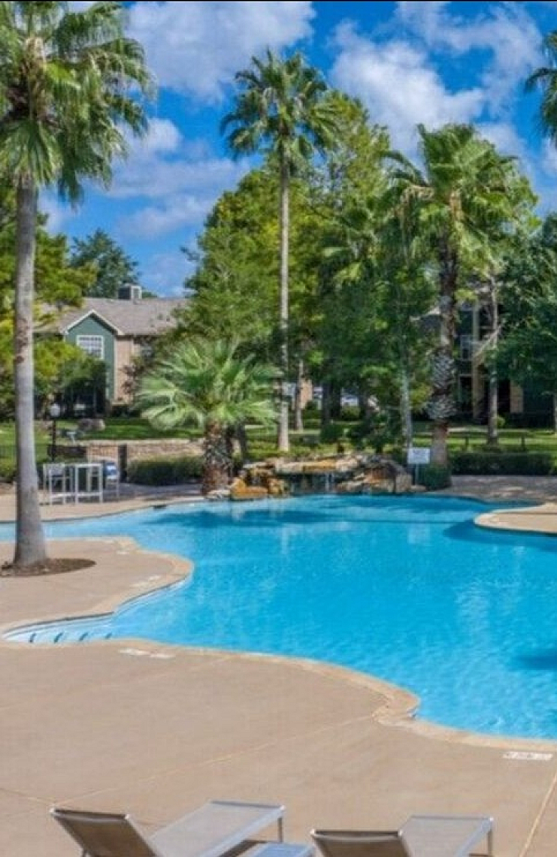 Inviting resort-style swimming pool surrounded by palm trees and greenery, perfect for relaxing and enjoying the sunny day.