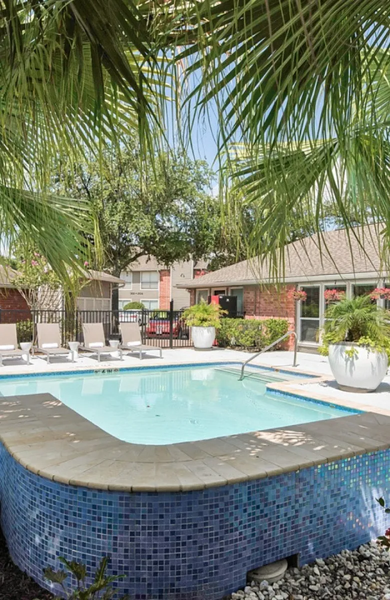 Inviting outdoor pool area with sun loungers, lush palm trees, and vibrant landscaping in a serene apartment community.