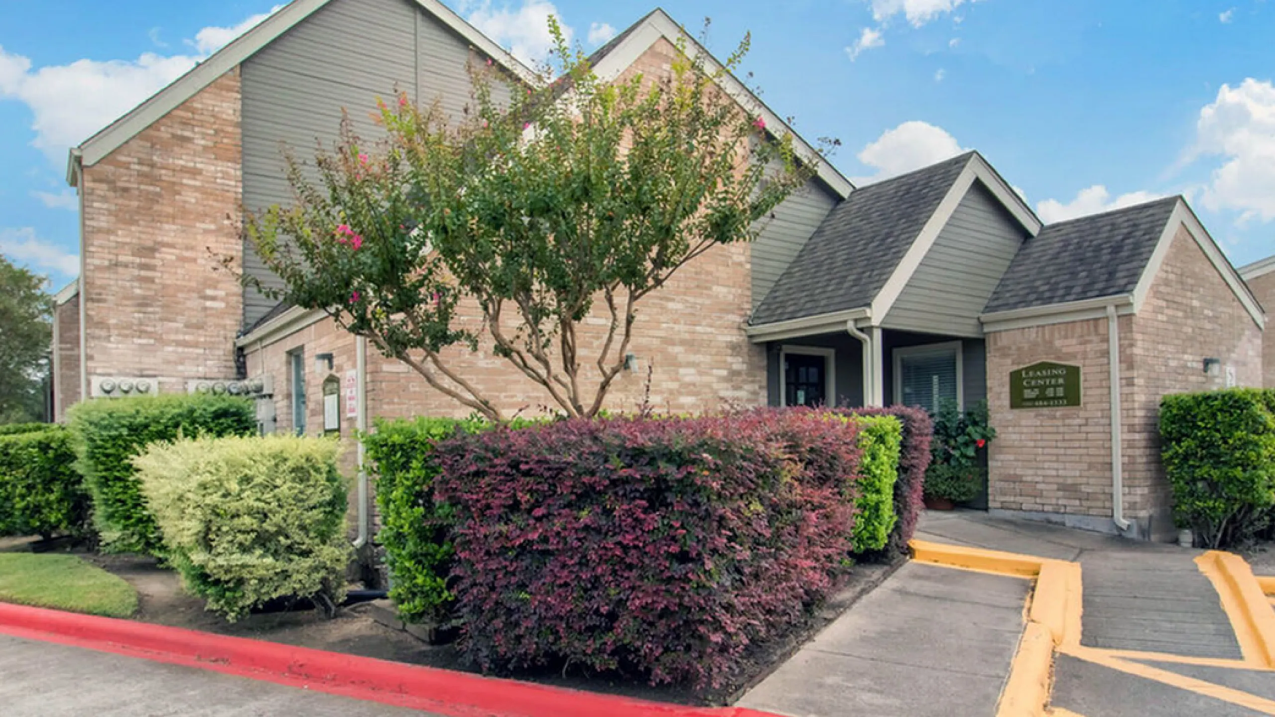 Charming apartment exterior featuring lush landscaping, brick facade, and inviting walkway.