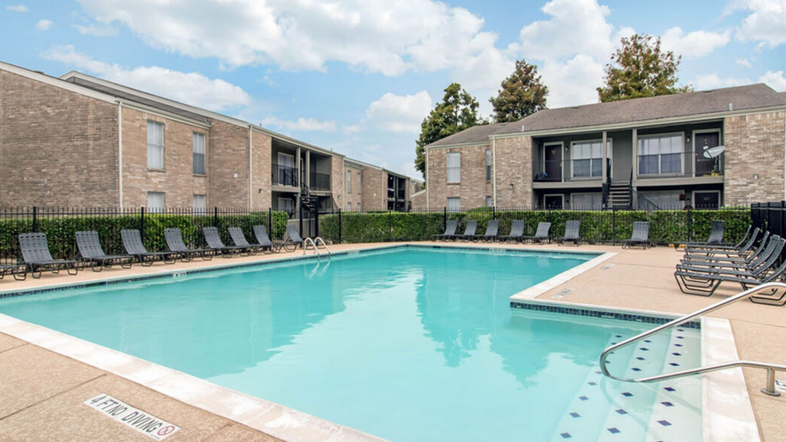 Inviting apartment community featuring a pristine swimming pool surrounded by elegant lounge chairs, perfect for relaxation and enjoyment.
