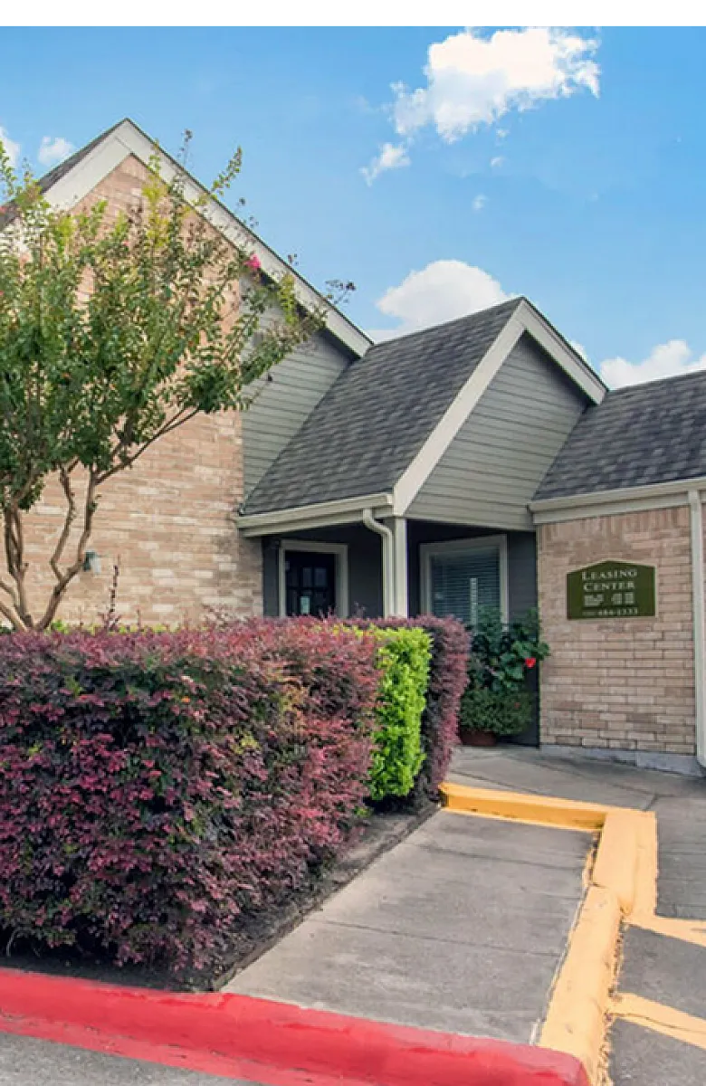 Charming brick apartment exterior with lush landscaping and a welcoming entrance under a clear blue sky.
