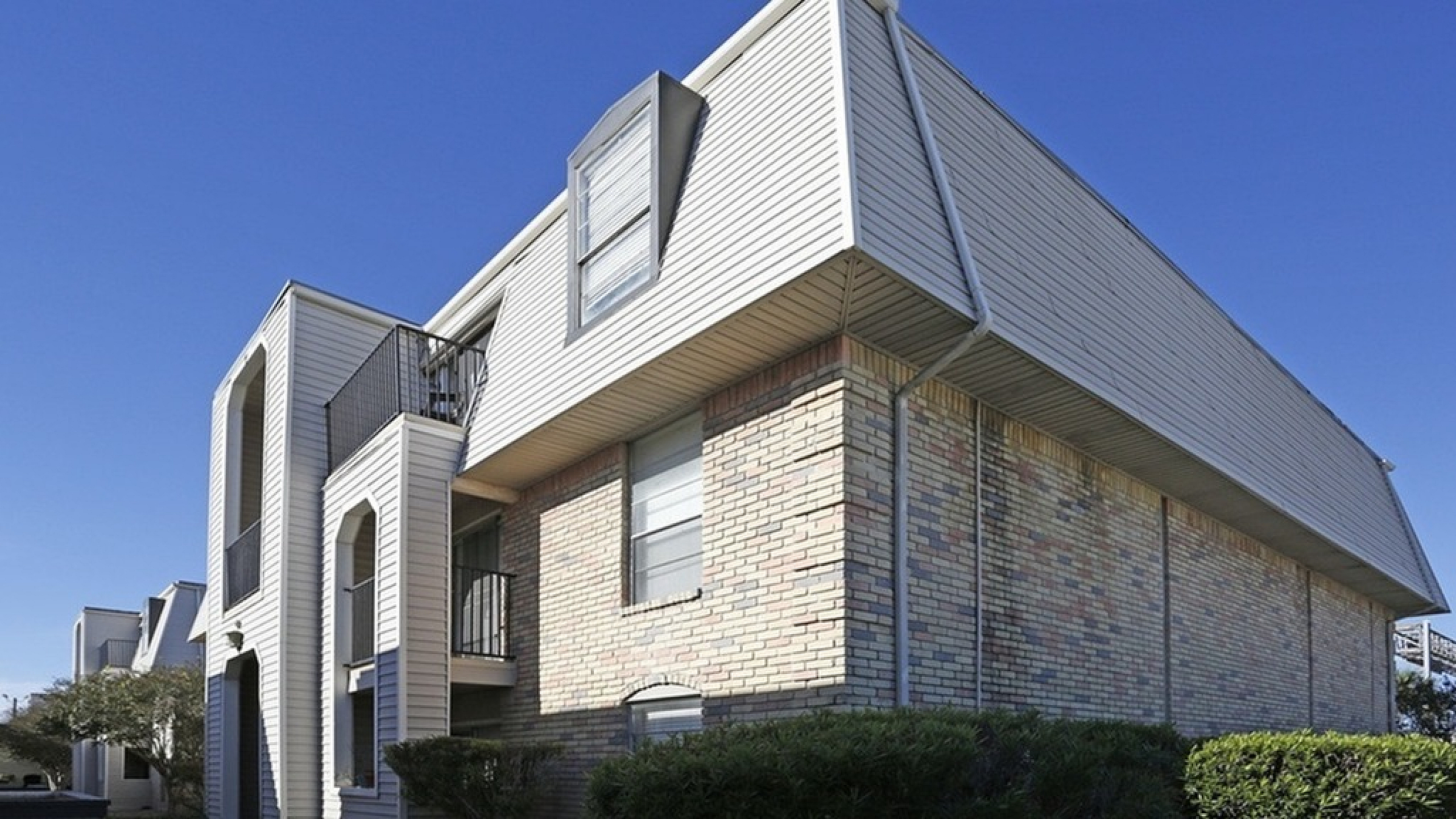 Charming apartment building with unique architectural angles, elegant brickwork, and serene landscaping against a bright blue sky.