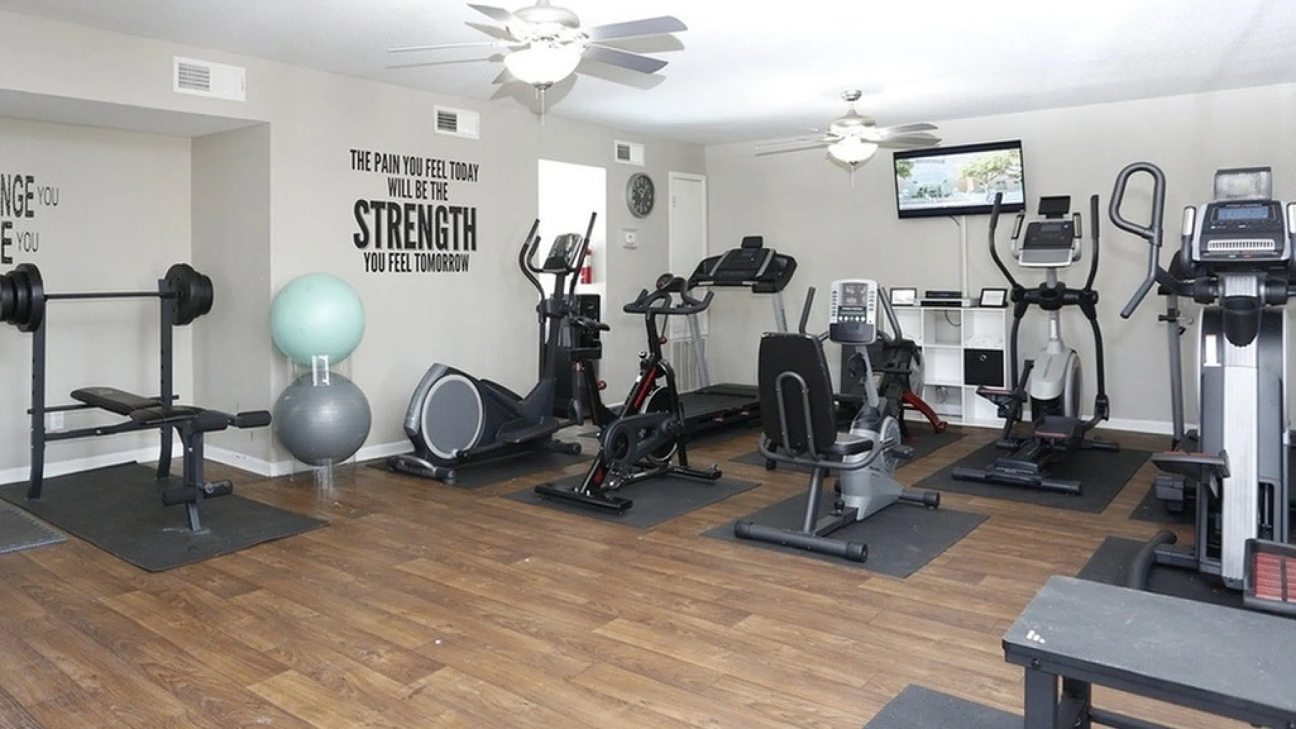 Modern apartment gym with state-of-the-art equipment, motivational wall quotes, and sleek wooden flooring.