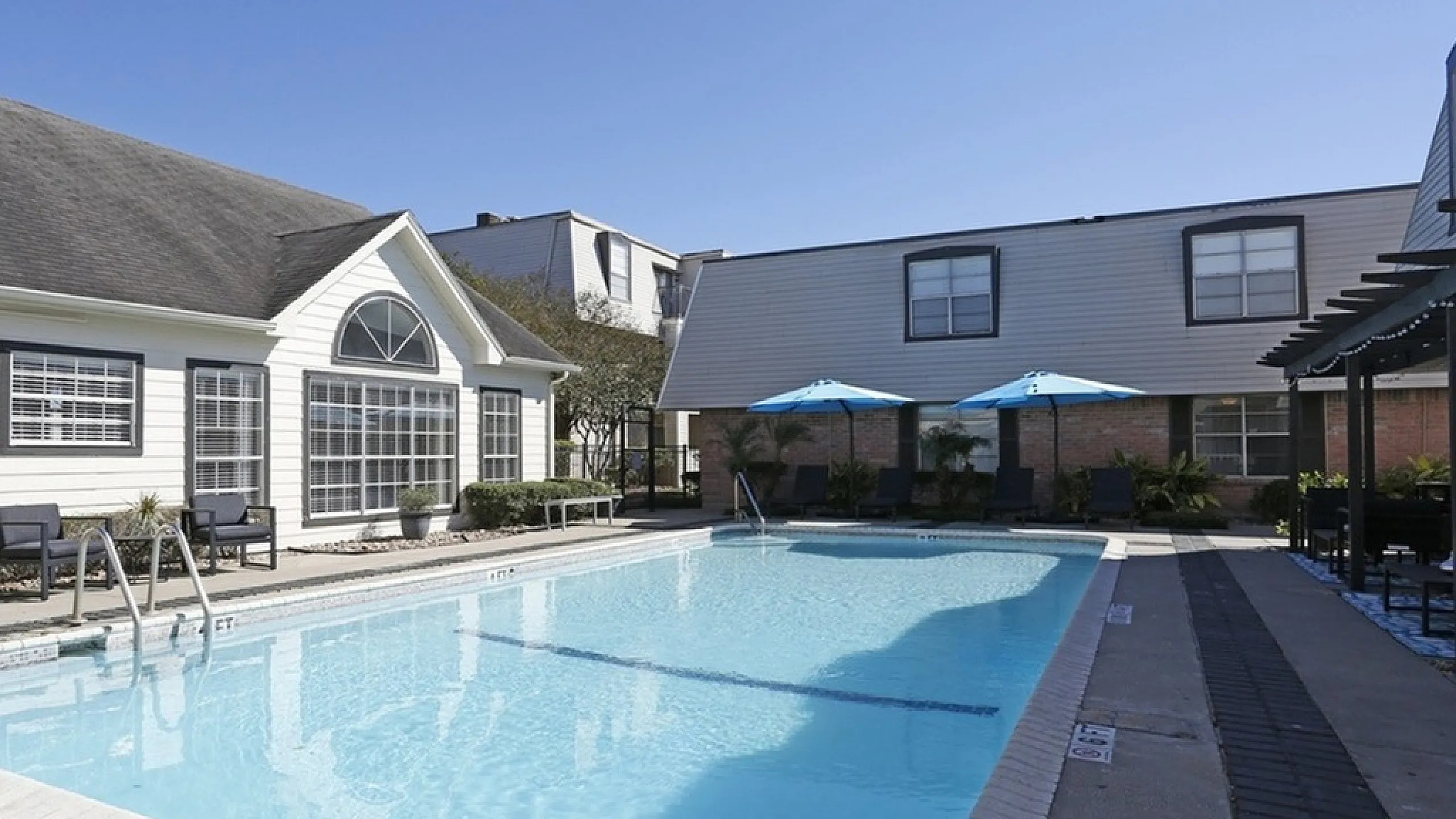 Inviting apartment complex with a sparkling outdoor pool, relaxing lounge chairs, and bright blue umbrellas, perfect for a sunny day retreat.