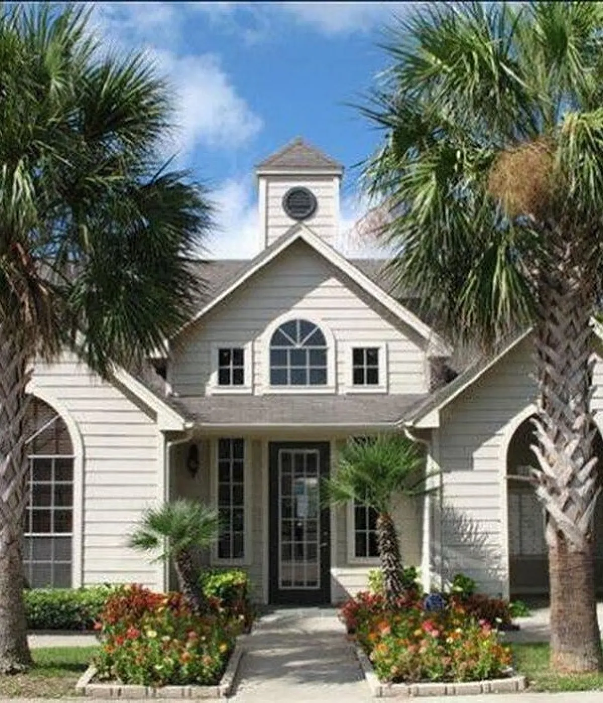 Charming home exterior with lush tropical landscaping and elegant arched windows, offering a warm and inviting atmosphere.
