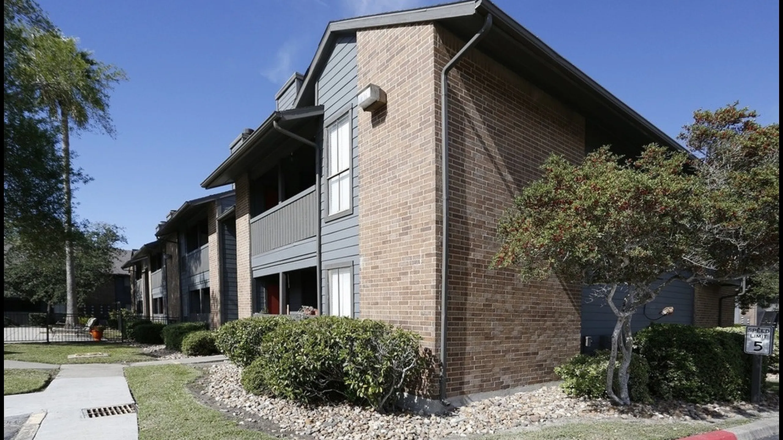 Charming residential building with brick facade and well-maintained landscaping under a clear blue sky.