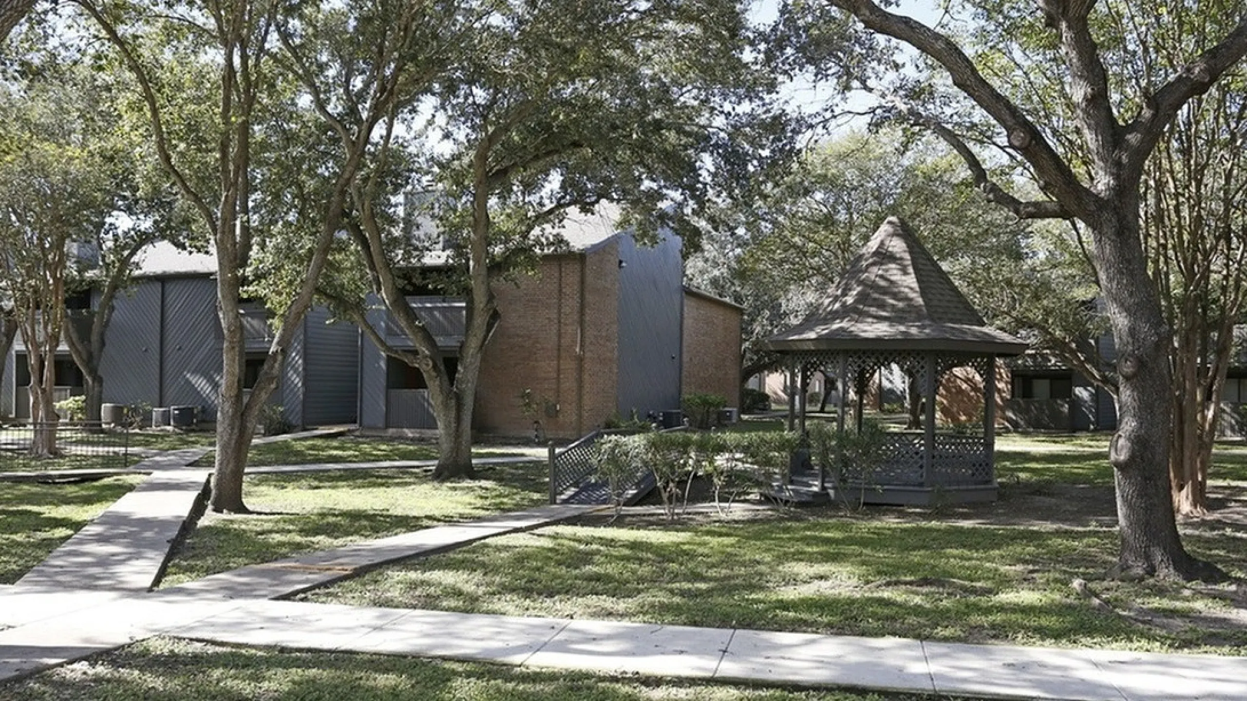 Charming apartment exterior with lush green landscaping and a cozy gazebo, showcasing tranquility and community living.