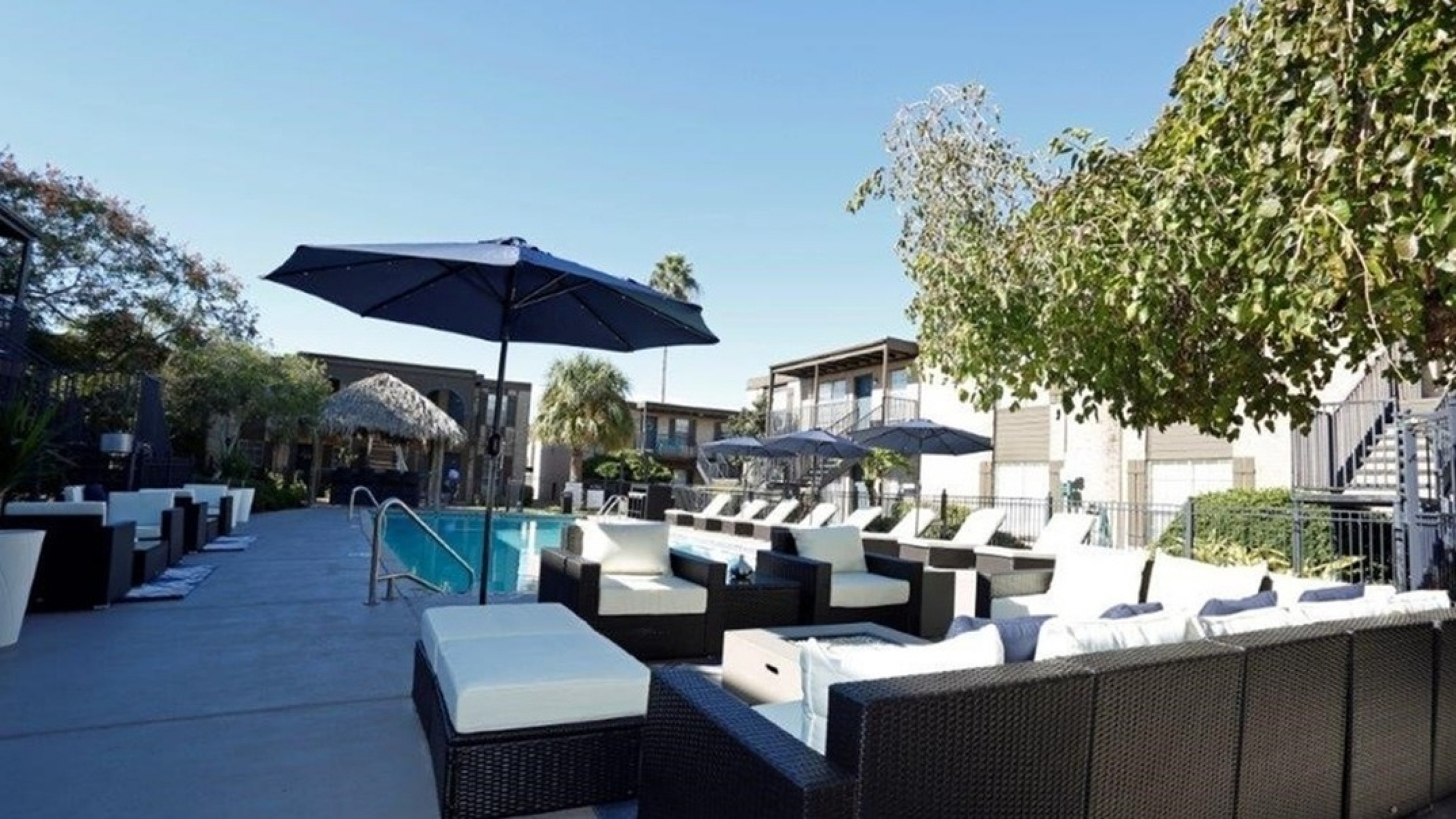 Luxurious outdoor pool area with modern lounge seating and umbrellas, surrounded by lush greenery and stylish architecture.