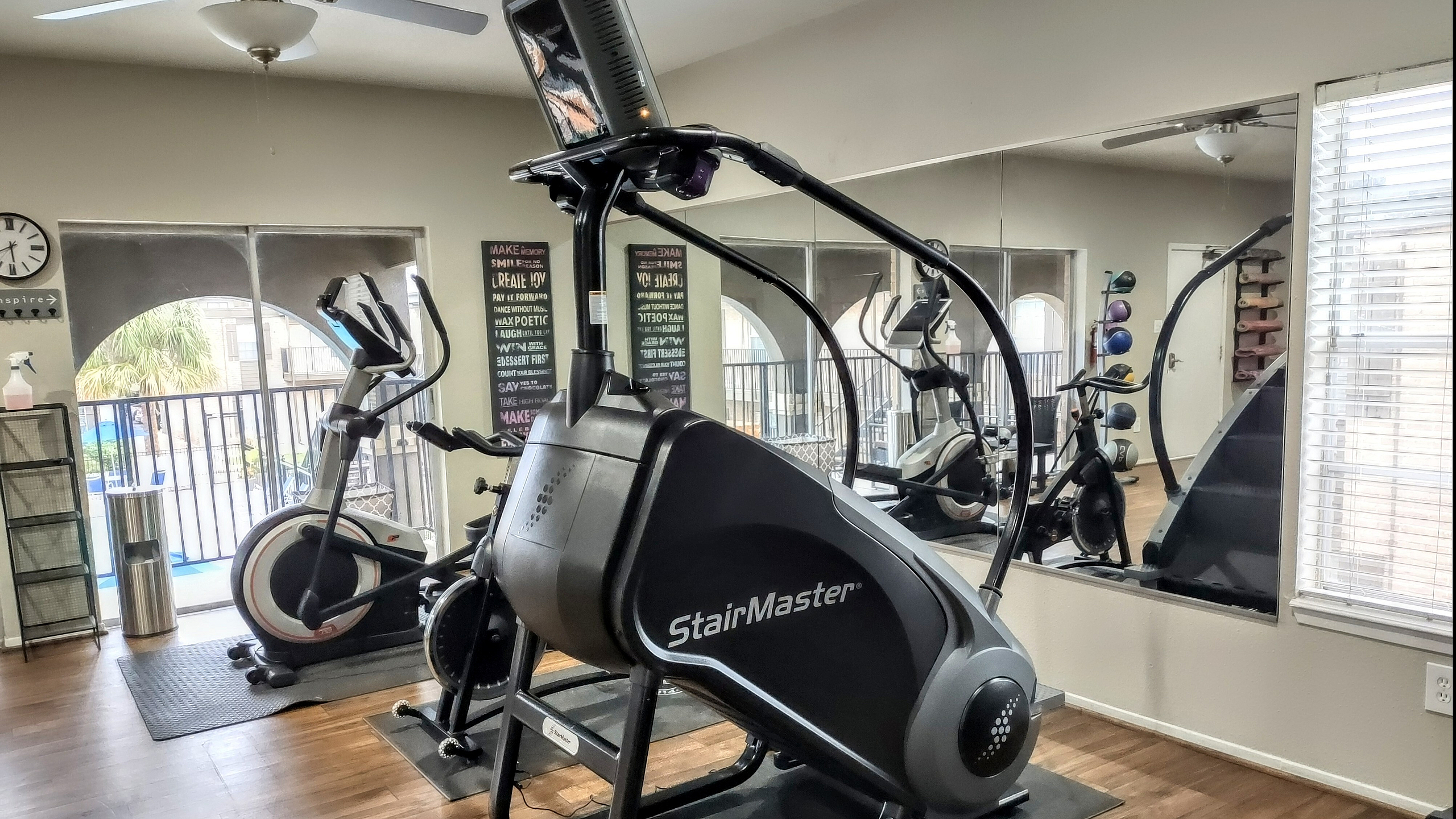 Modern fitness center featuring a StairMaster and exercise bikes in a bright, spacious room with wood flooring and mirrors.