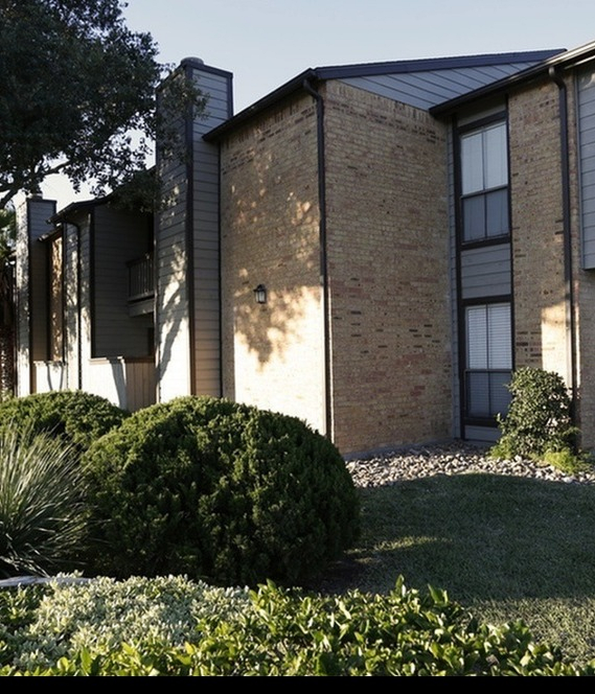 Charming brick apartment exterior with modern accents, nestled among lush greenery and serene landscaping.