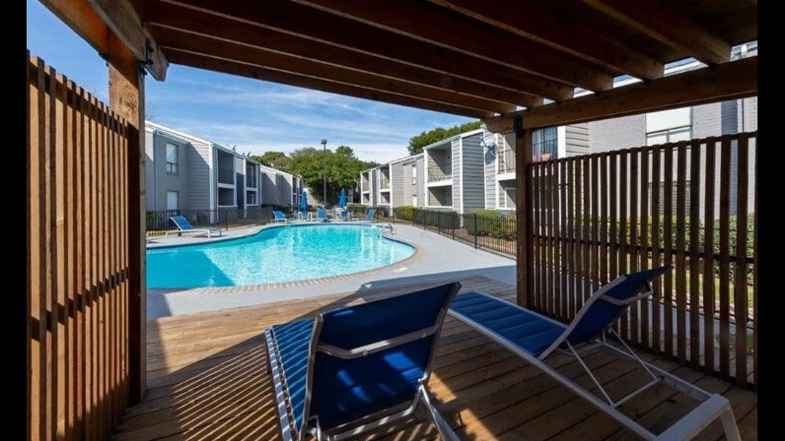Beautiful apartment complex with a sparkling pool and shaded lounge area, perfect for relaxation and leisure in a tranquil setting.