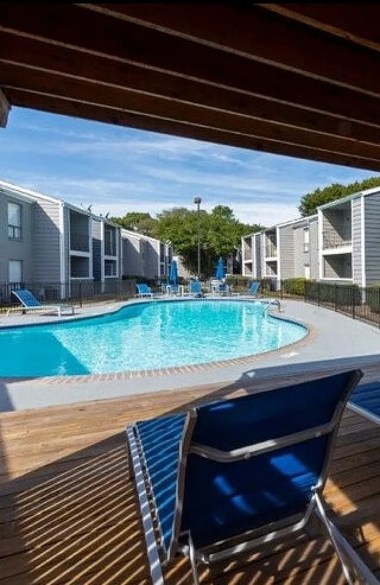 Inviting apartment complex pool area with lounge chairs under a wooden pergola, perfect for relaxation.