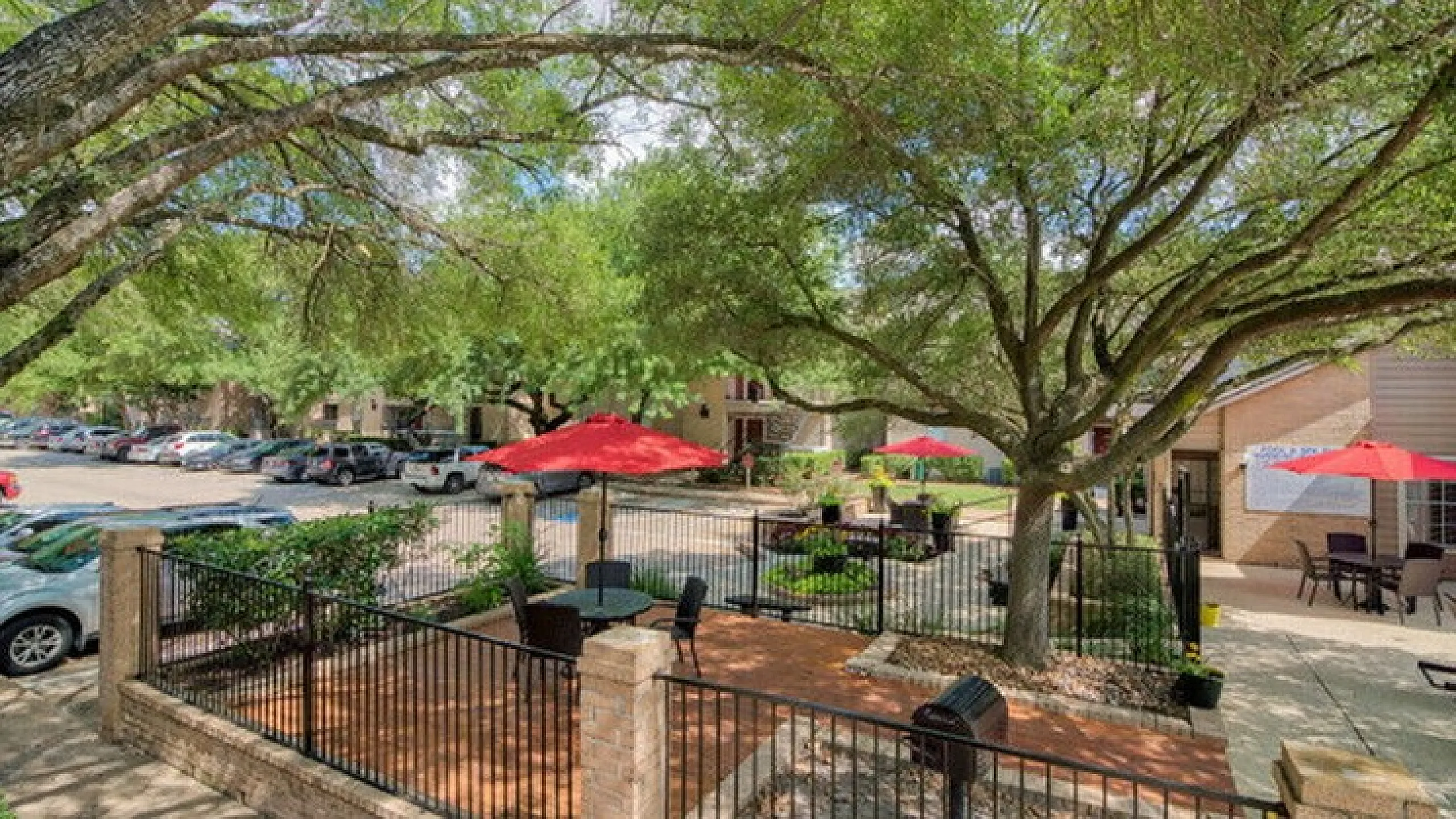 Charming outdoor patio featuring lush greenery, vibrant red umbrellas, and modern seating, ideal for relaxation and gatherings.