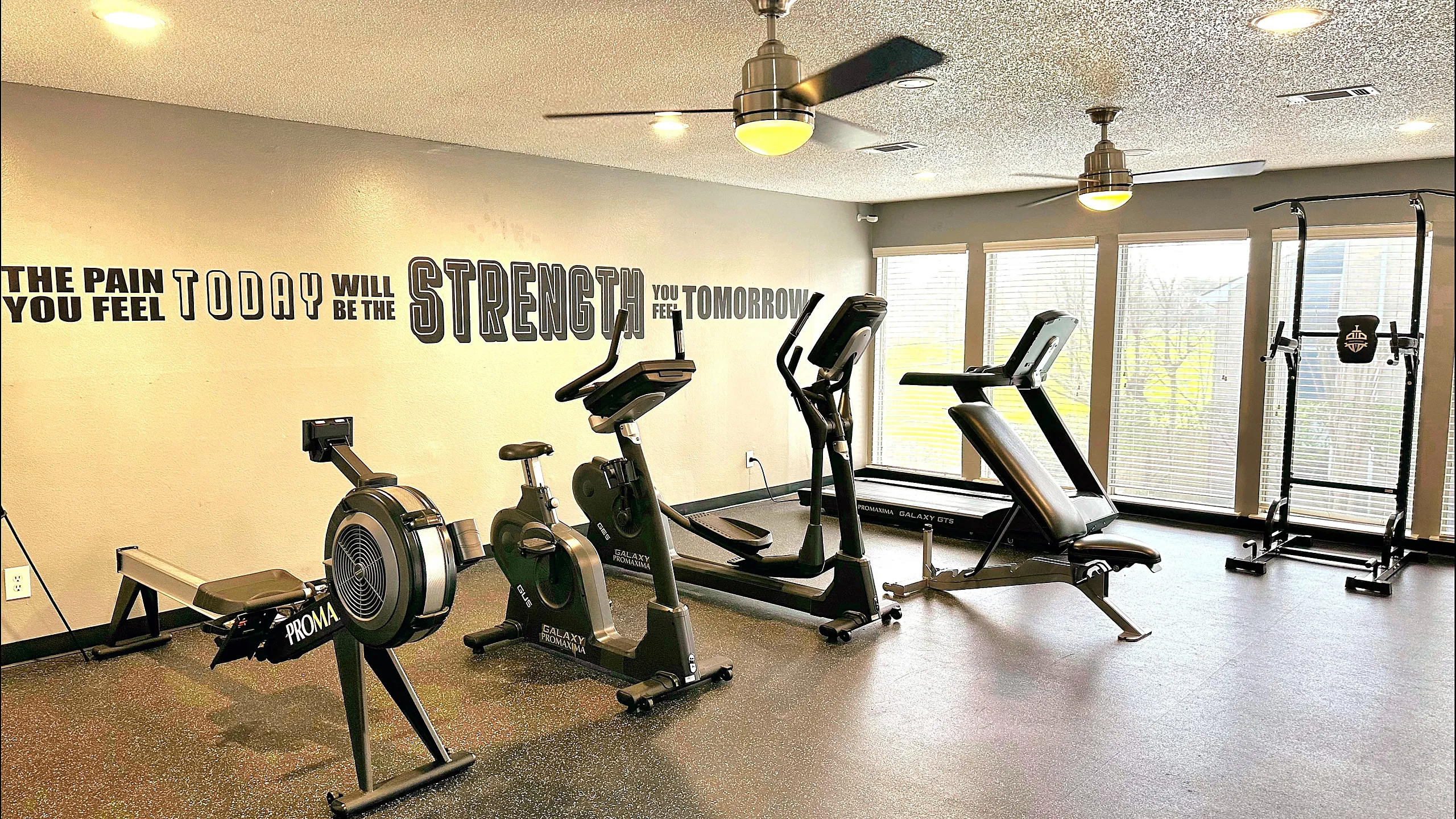 Modern fitness center with exercise equipment, motivational wall art, and large windows for natural light.