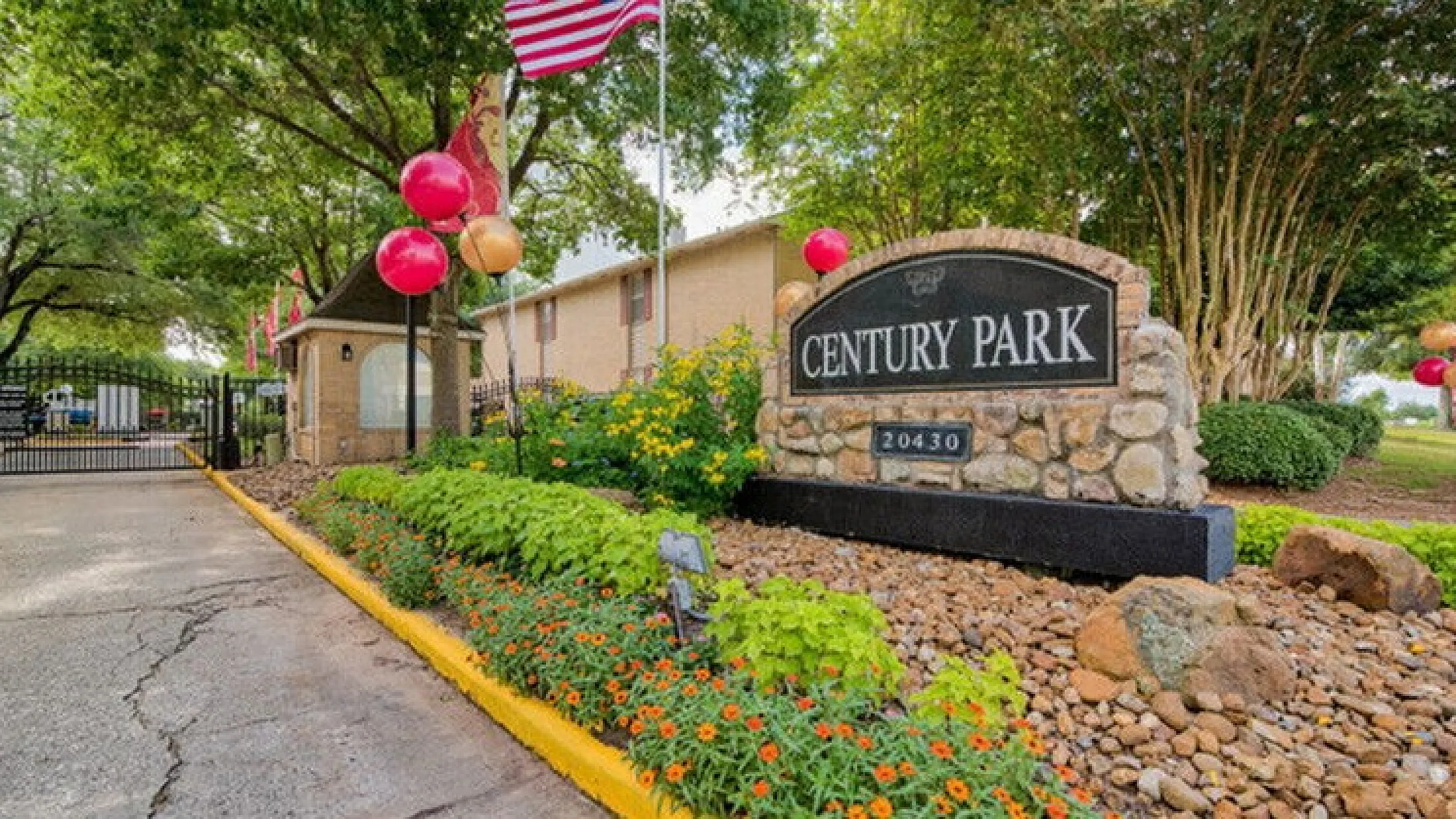 Inviting entrance of Century Park apartment community with lush landscaping and vibrant flowerbeds under a clear sky.
