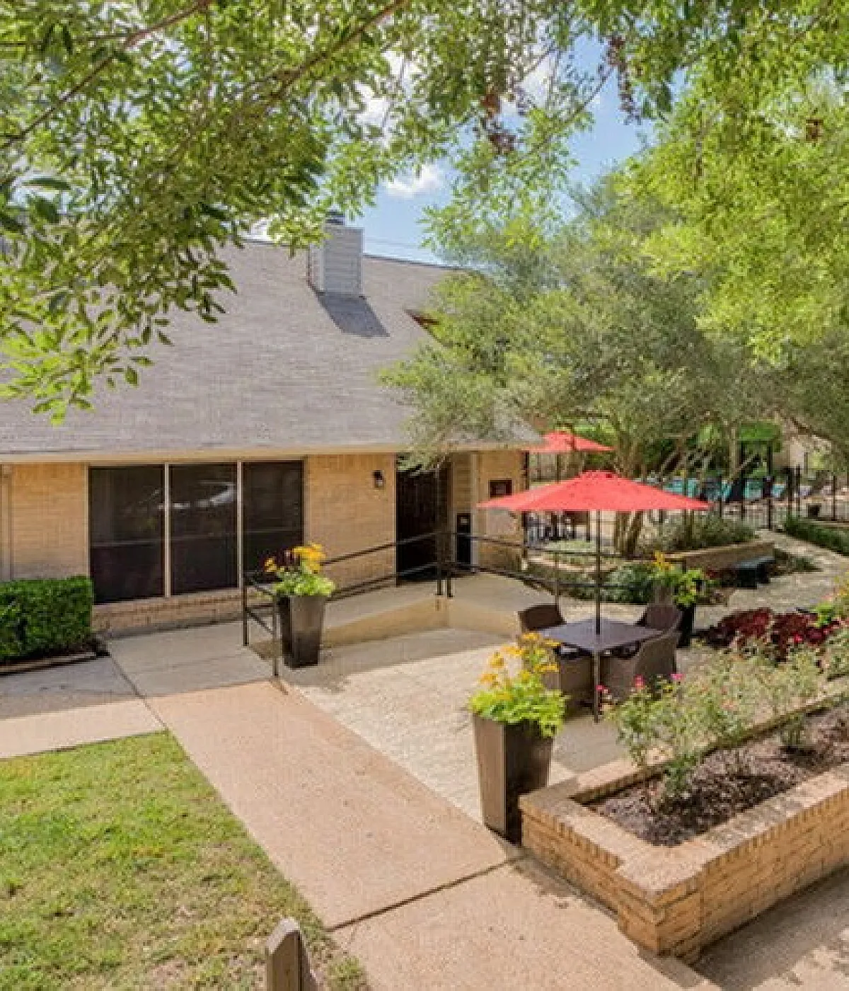 Charming outdoor patio area surrounded by lush greenery, featuring cozy seating and vibrant red umbrellas, perfect for relaxation and entertaining.