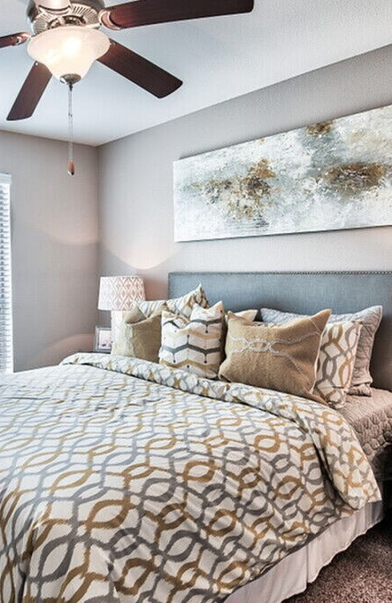 Charming bedroom with cozy decor, featuring a plush bed, elegant patterned bedding, modern ceiling fan, and natural light streaming through a large window.