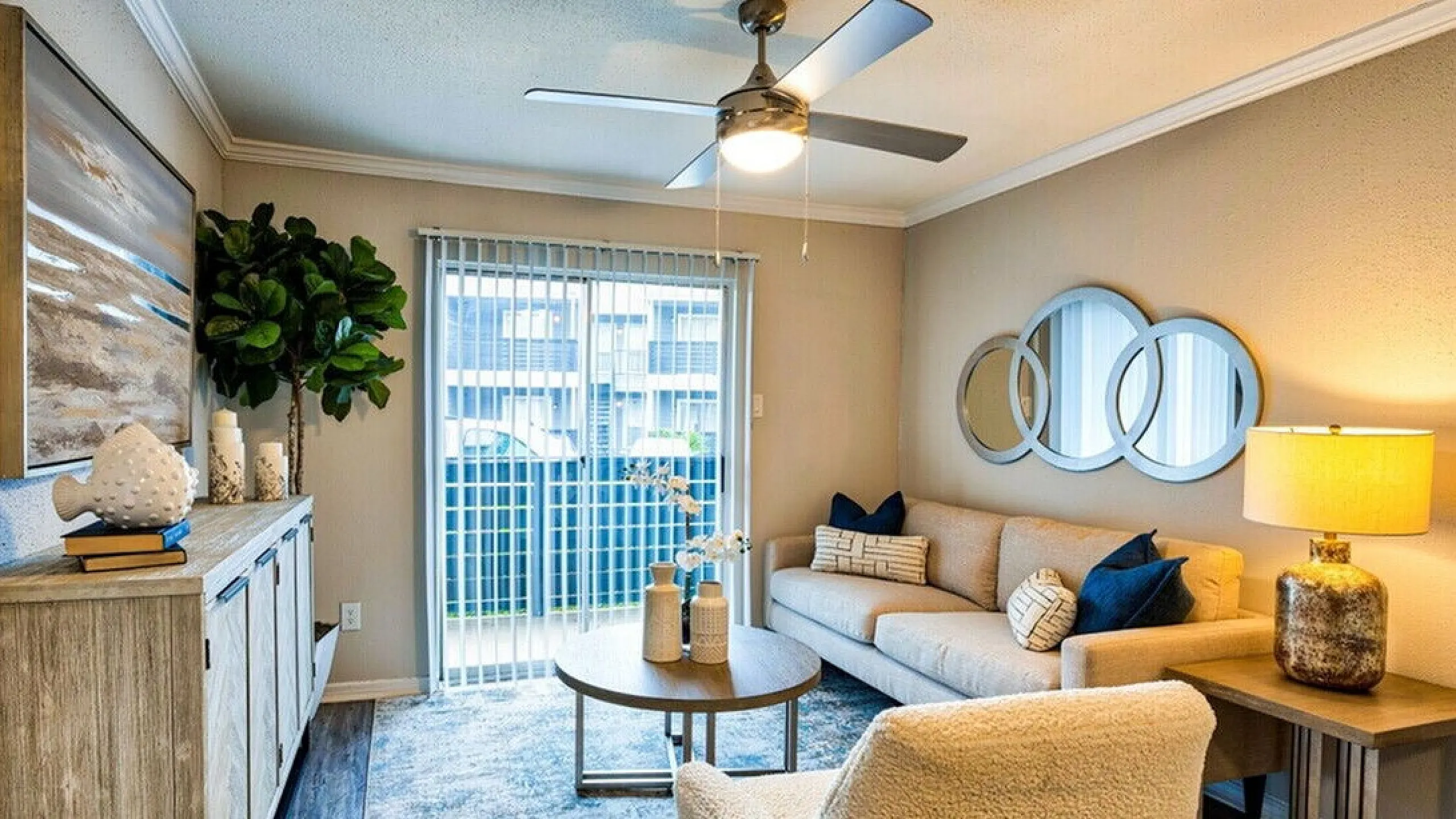 Cozy modern living room with elegant decor, plush beige sofa, stylish coffee table, and natural light streaming through large glass doors.